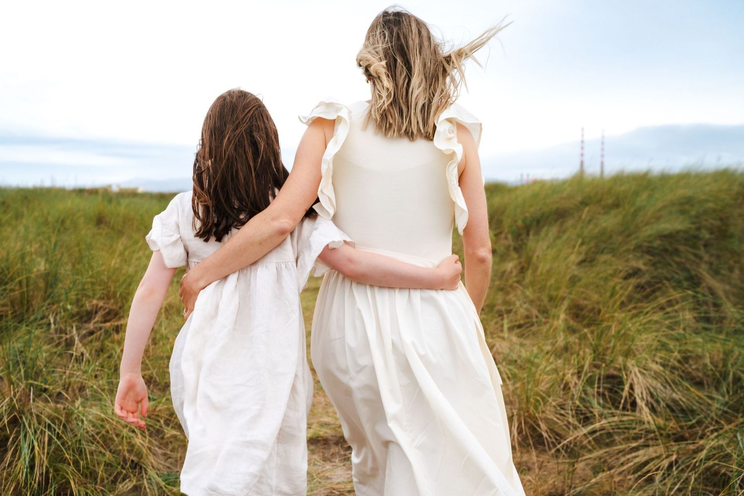 Two people walking hand in hand through a scenic field with tall grass at sunset.  Family photographer Dublin Ireland  Family photographer D