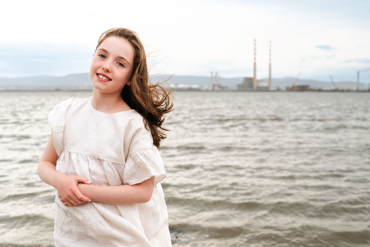 Triptych photo series showing someone in a white dress smiling against a cloudy oceanfront background.  Family photographer Dublin Ireland