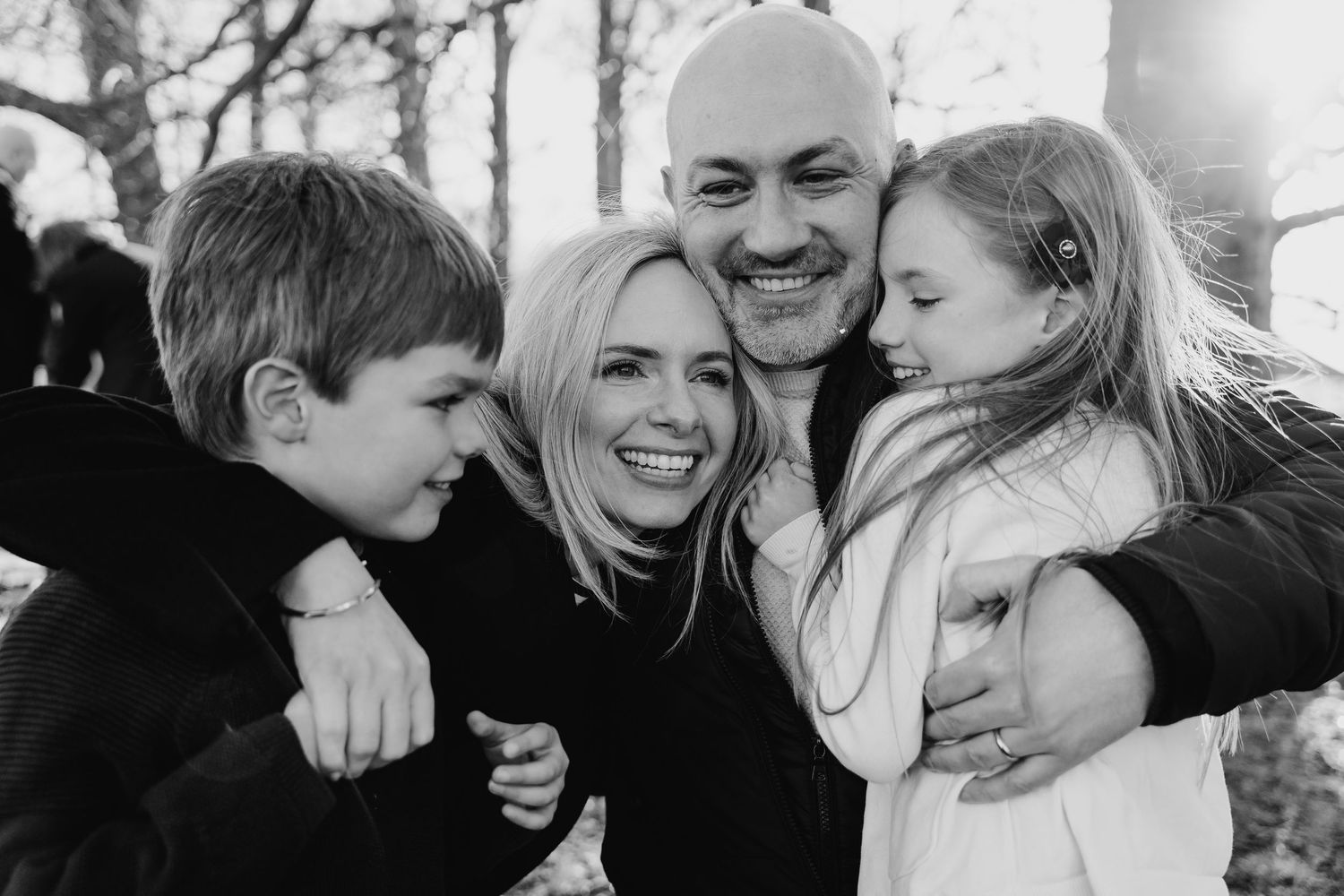 Black and white portrait of a happy family of four embracing and laughing together outdoors. family PHOTOGRAPHER Dublin