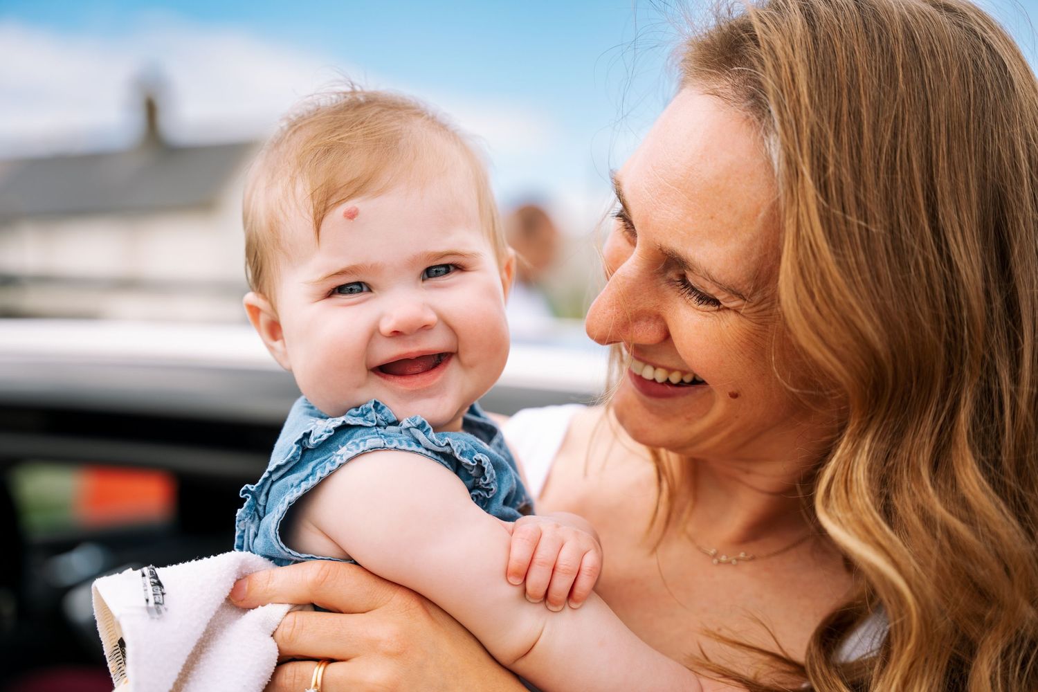A joyful moment of shared laughter between parent and baby wearing denim against a blurred outdoor background. family PHOTOGRAPHER Dublin