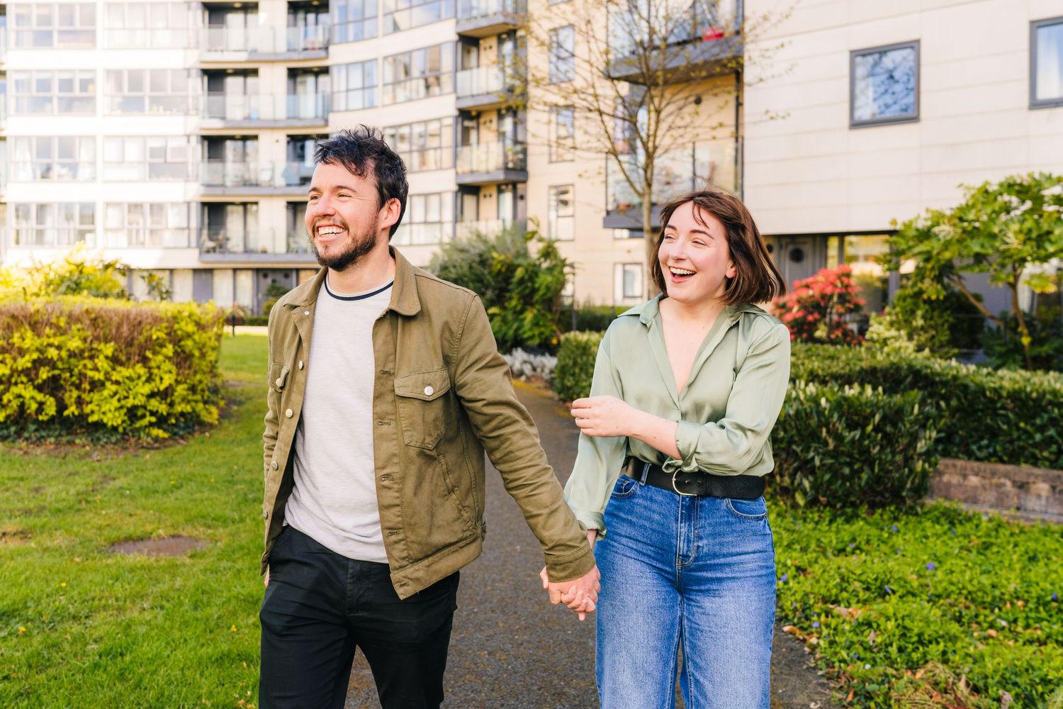 A cheerful couple enjoying a walk together along an urban path with apartment buildings and greenery in the background. PHOTOGRAPHER Dublin
