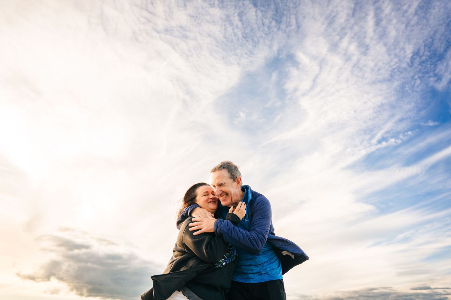 A couple embraces at sunset against a dramatic cloudy sky with soft blue and white colors. PHOTOGRAPHER Dublin ireland