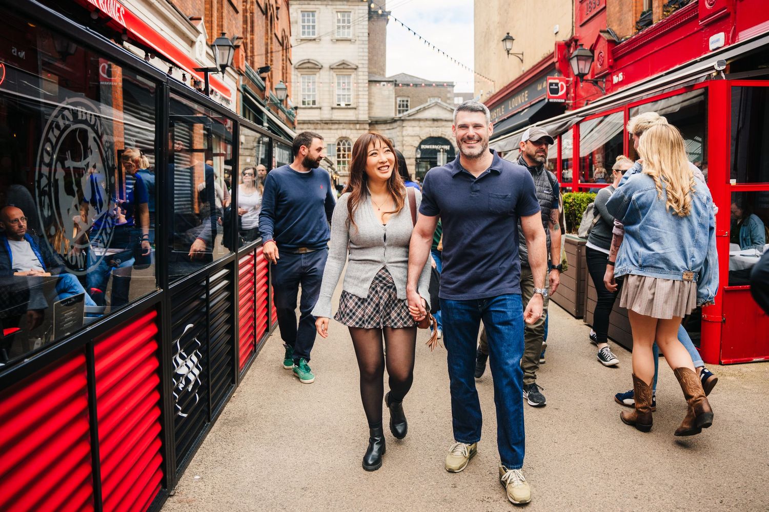 People stroll through a lively market street with red awnings and storefronts in an urban setting. PHOTOGRAPHER Dublin