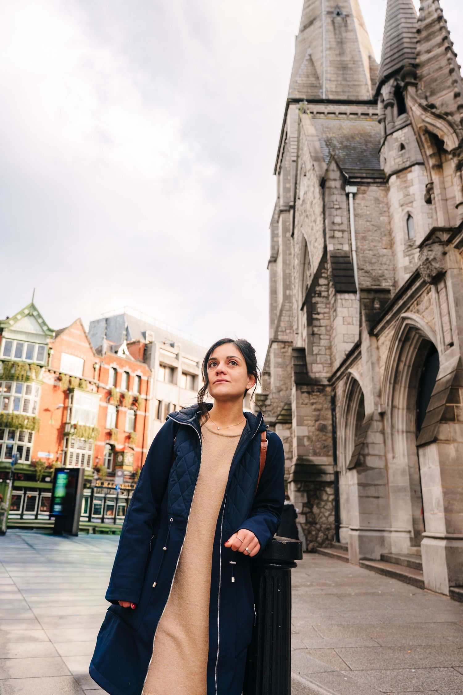 Person in a navy blazer and beige top poses thoughtfully against gothic church architecture in an urban setting. professional headshots dubl