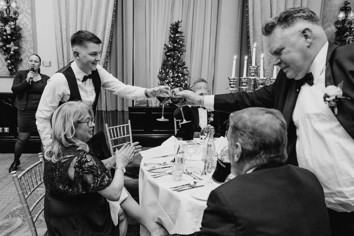 Black and white photo of waiters serving guests at elegant holiday dinner with Christmas tree. Wedding photographer dublin