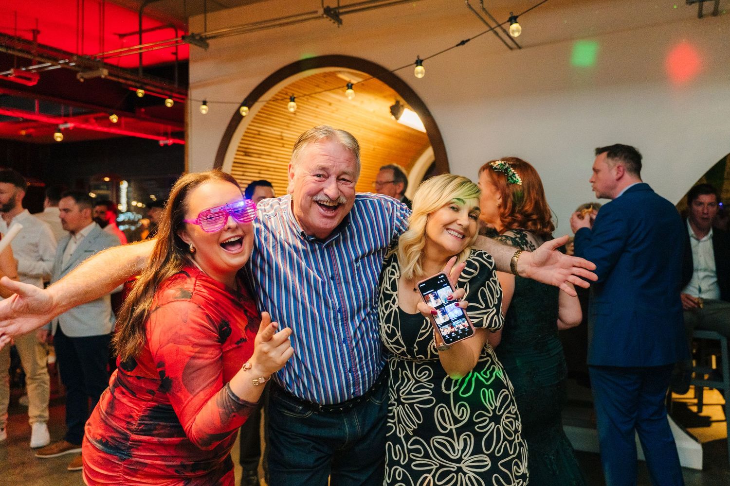 Guests dancing and celebrating with enthusiasm at an indoor event with red and white lighting. Dublin wedding photogrAPher
