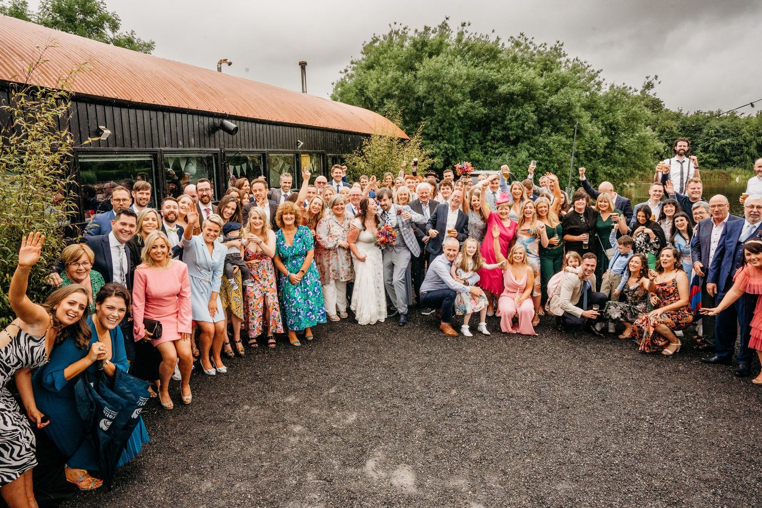Wide panoramic view of wedding guests lined up for a group photo at an outdoor venue. Wedding photographer Dublin