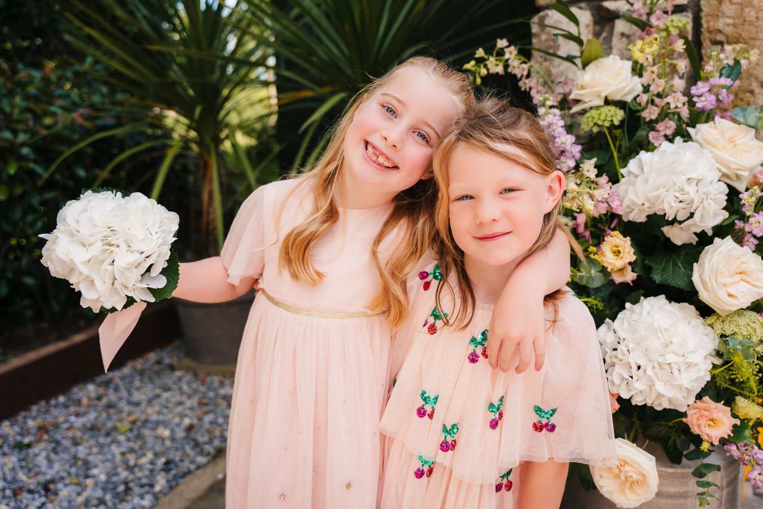 Two young girls in pink dresses laughing together among floral decorations. . Village Barn Tyrrellspass wedding photographer Ireland
