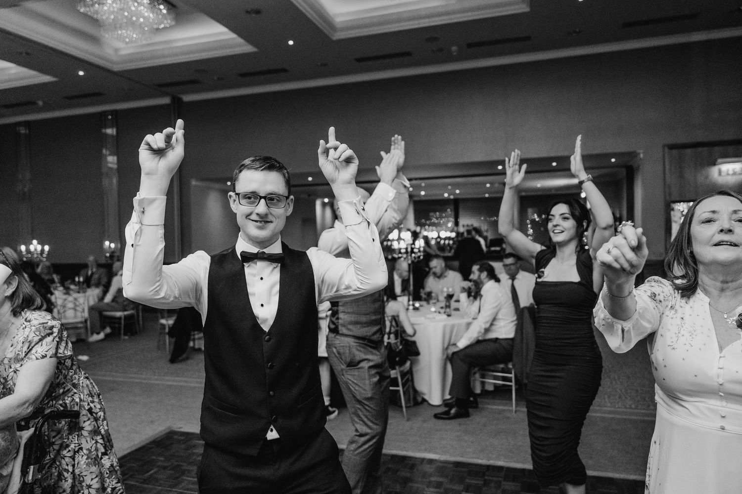 Black and white photo of wedding guests dancing with arms raised on the dance floor.  Wedding PHOTOGRAPHER Trim Castle