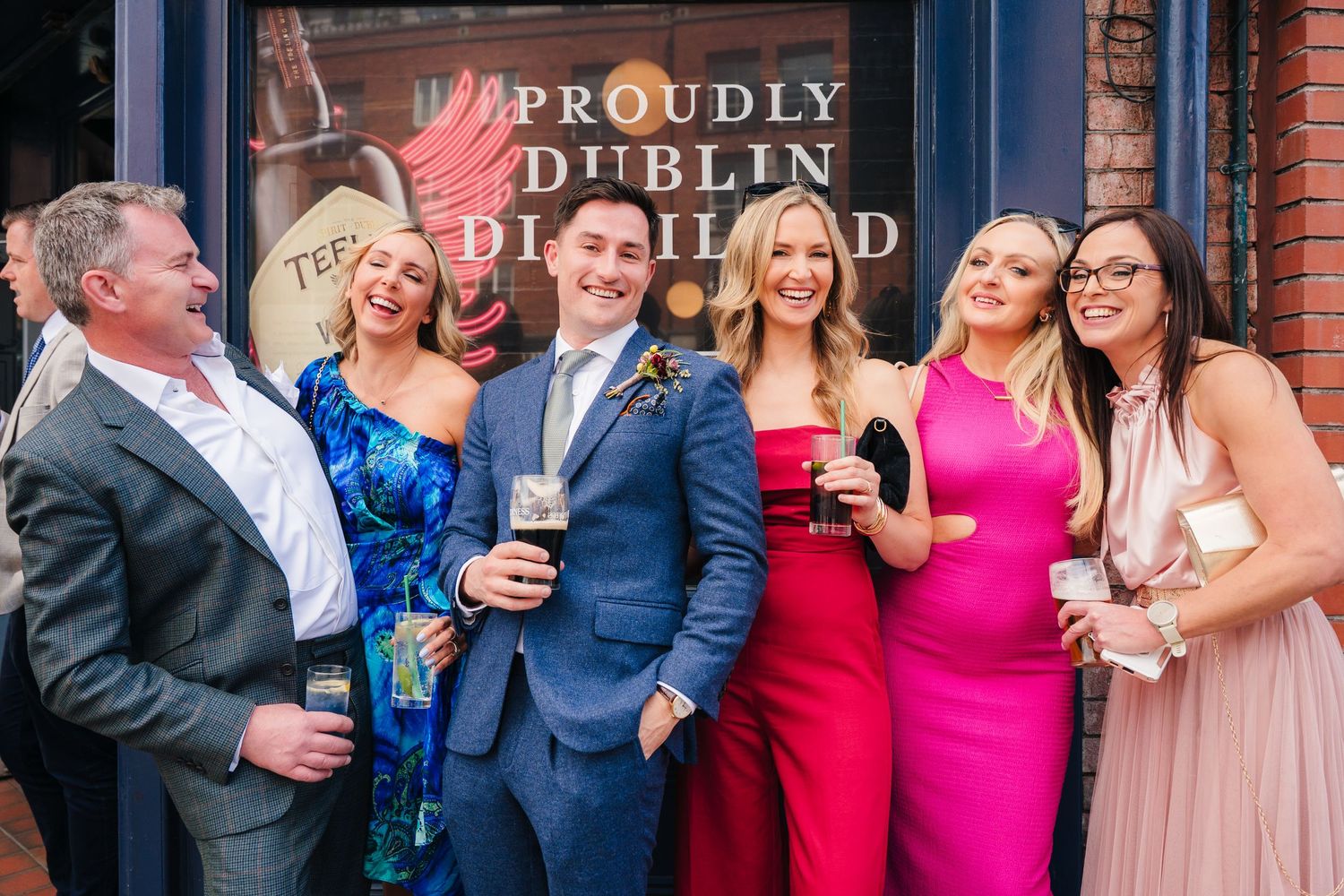 Wedding party poses against red brick wall outside Dublin pub. Same sex wedding PHOTOGRAPHER Dublin