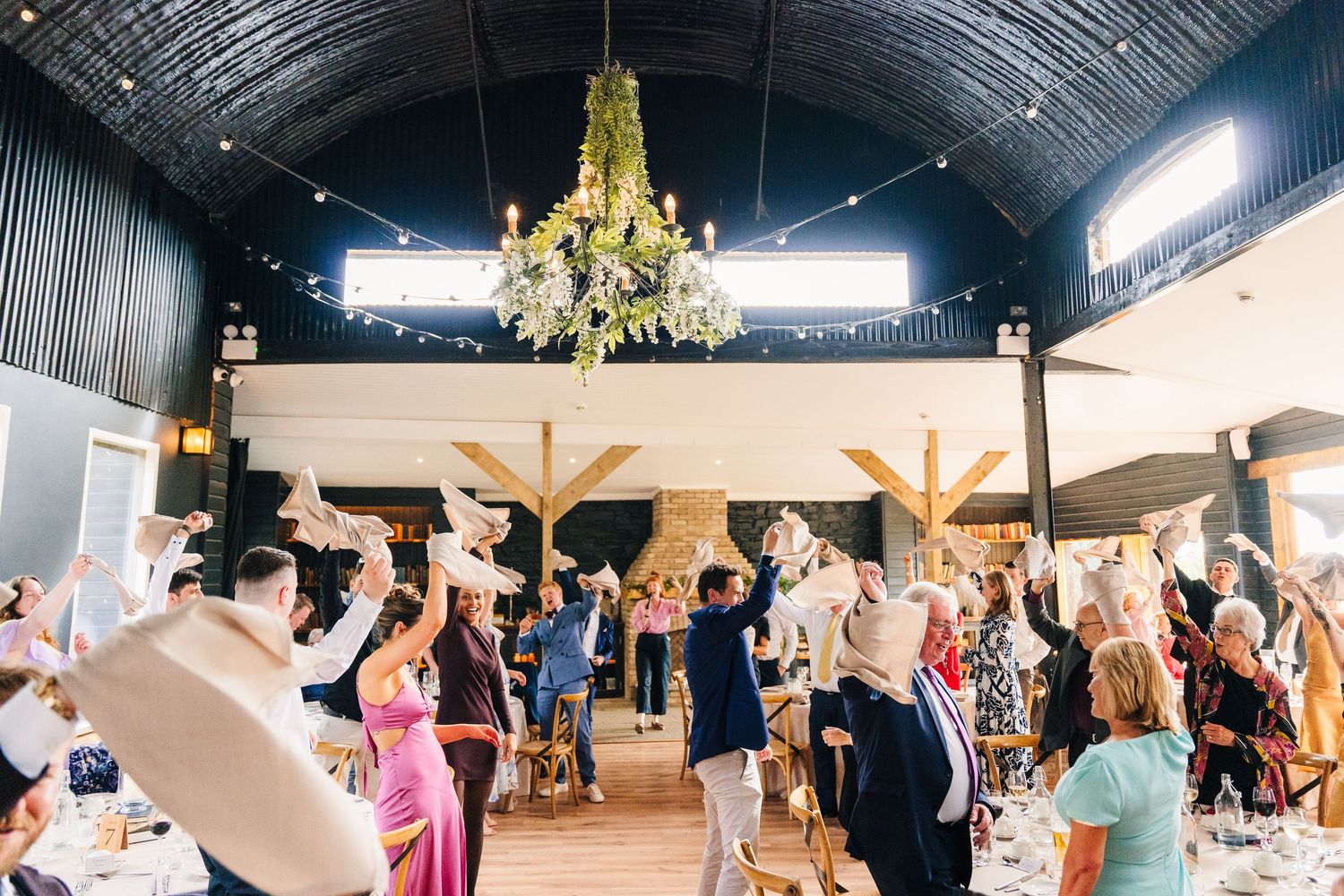 Poulaphouca Wedding photographer wicklow  Wedding guests dancing under golden chandelier in rustic venue.