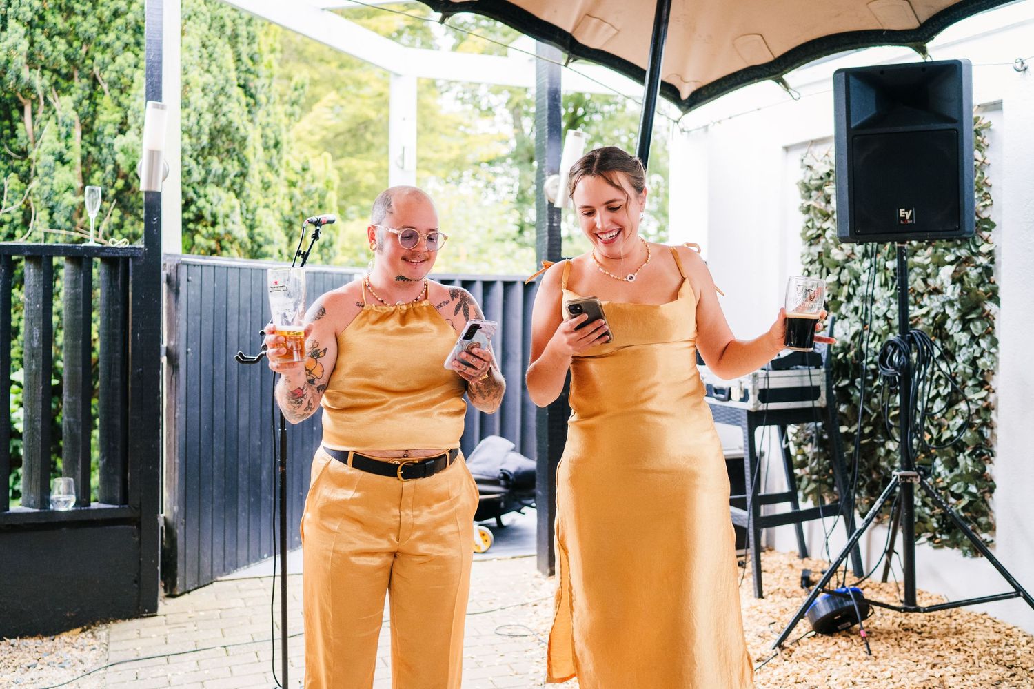 Poulaphouca Wedding photographer wicklow  Two wedding guests in matching yellow outfits checking their phones under umbrella.
