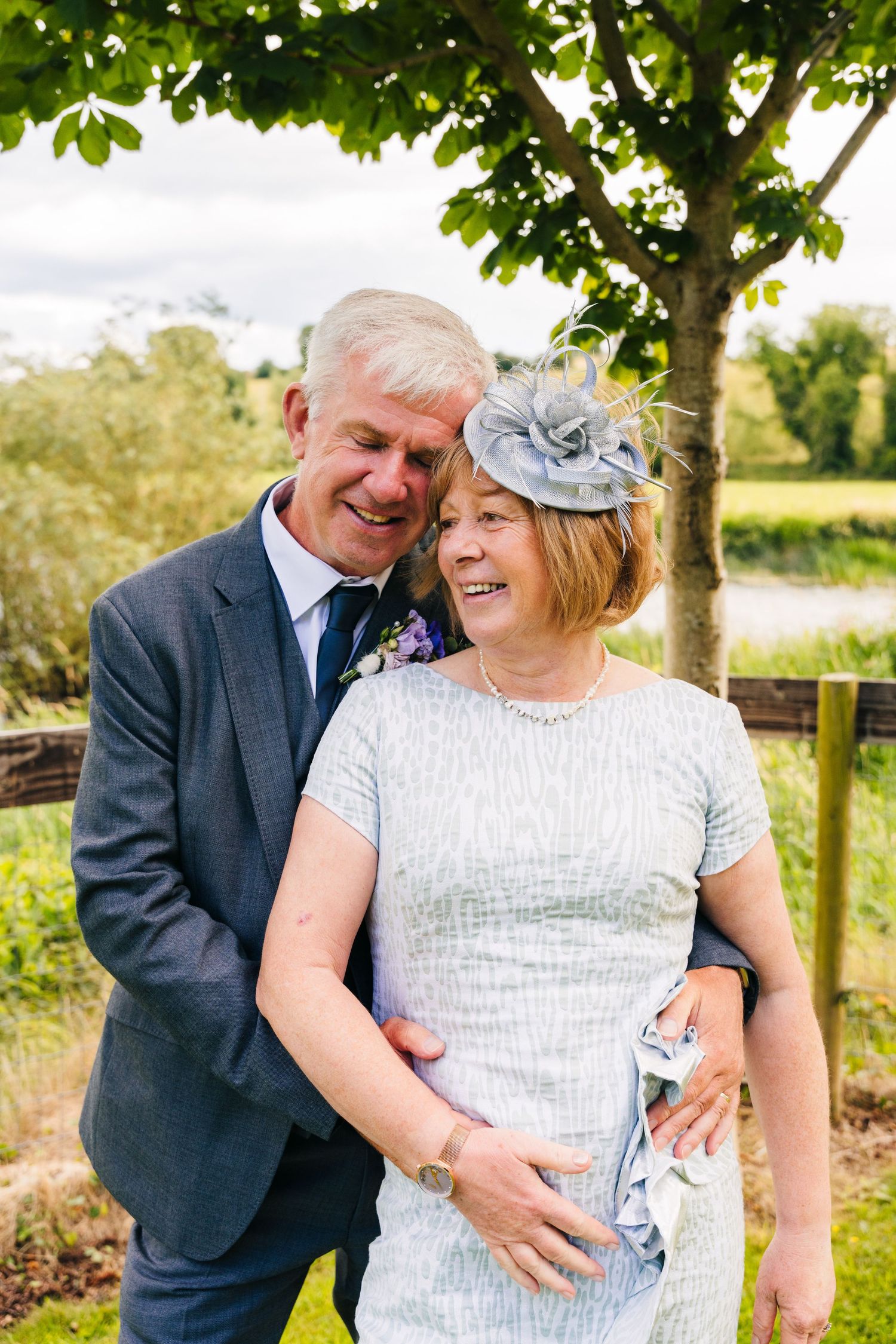 Millhouse slane wedding photographer dublin A couple embraces and laughs together in a garden setting with a tree in the background.
