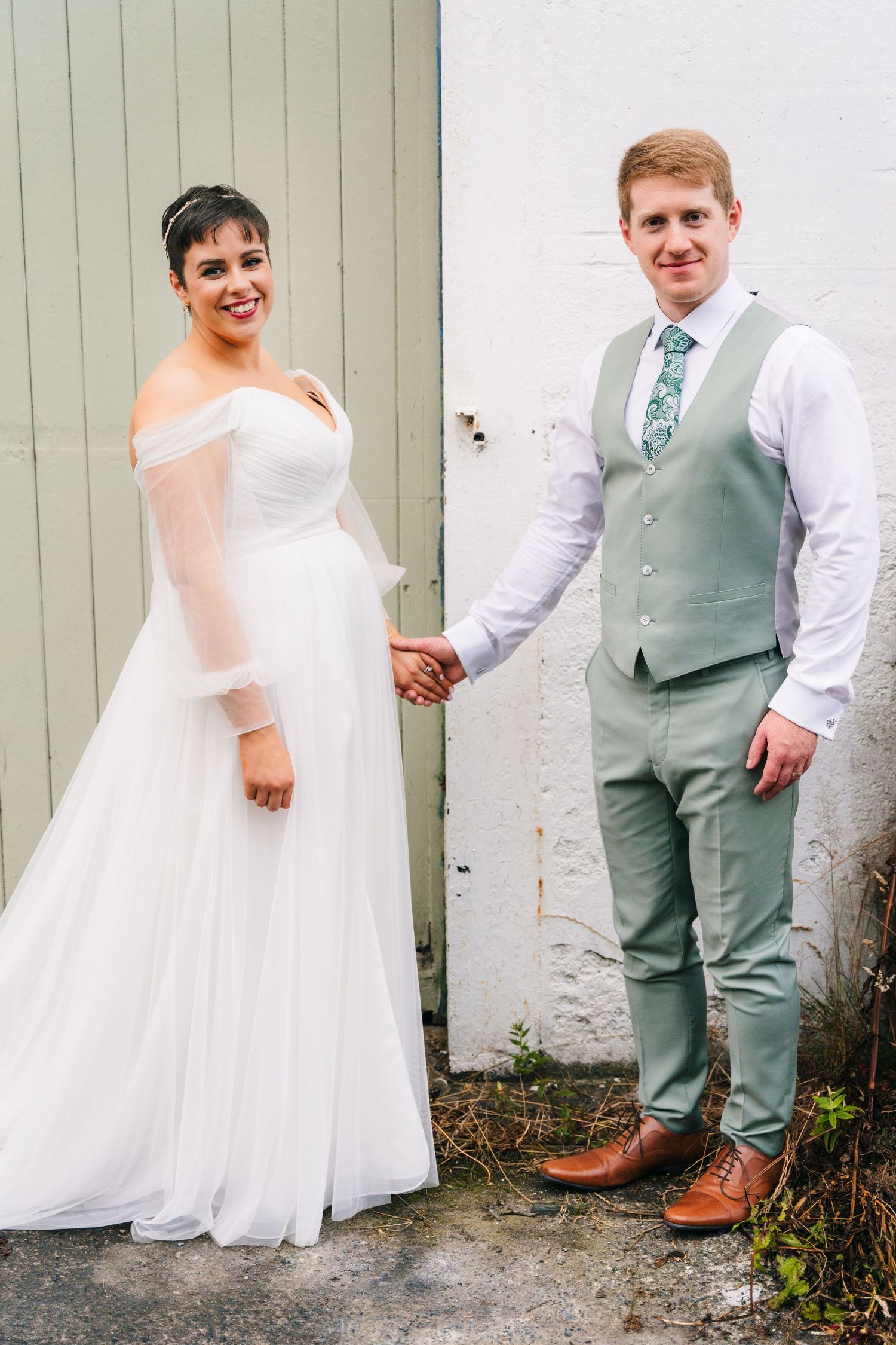 Millhouse slane wA bride in an off-shoulder white gown holds hands with their partner wearing a mint green vest and tie at an outdoor venue.
