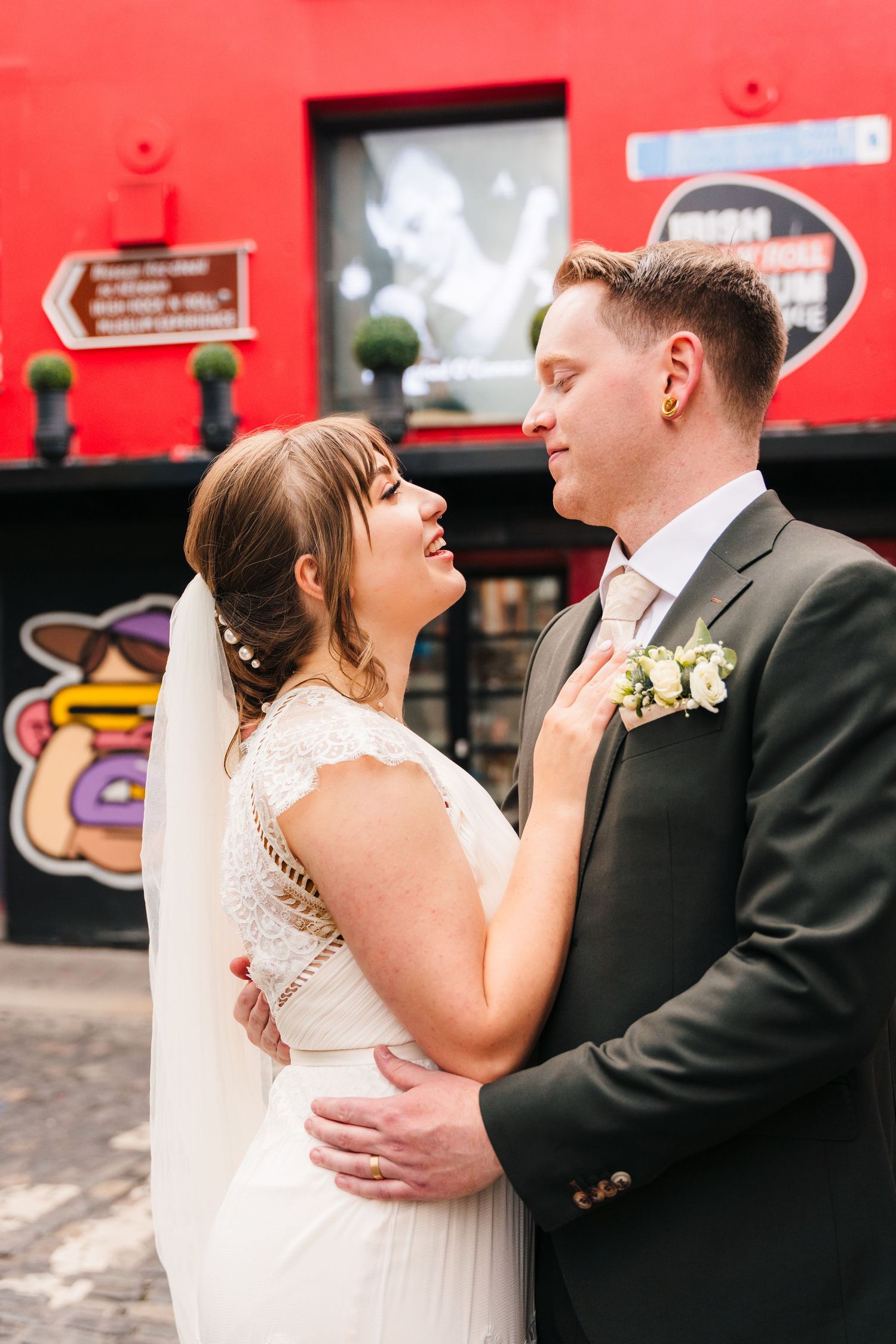 A romantic wedding portrait against a vibrant red wall with urban signage in the background. PHOTOGRAPHER Dublin Ireland Wedding