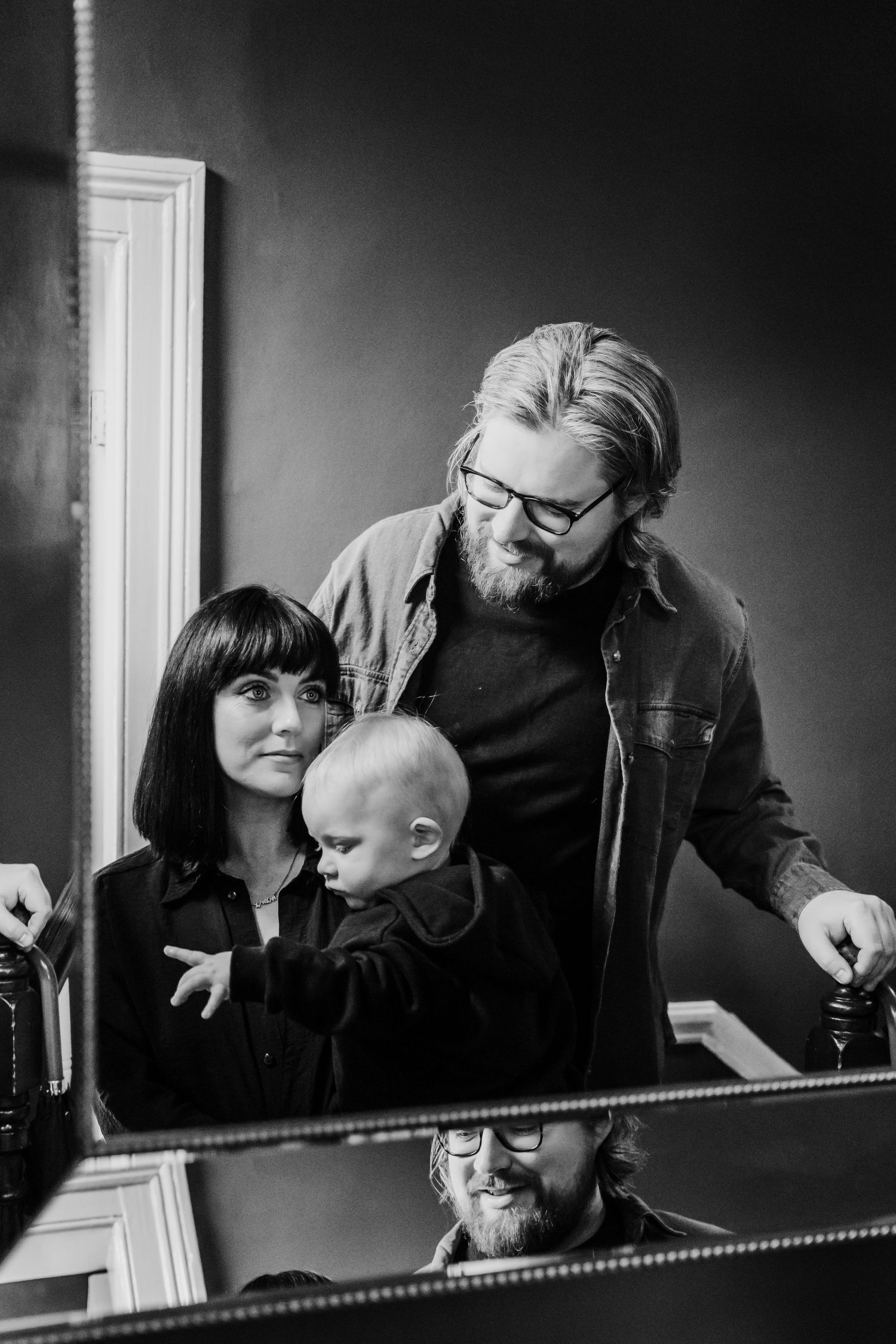 A candid black and white family portrait captured in front of a mirror.  Family PHOTOGRAPHER Dublin