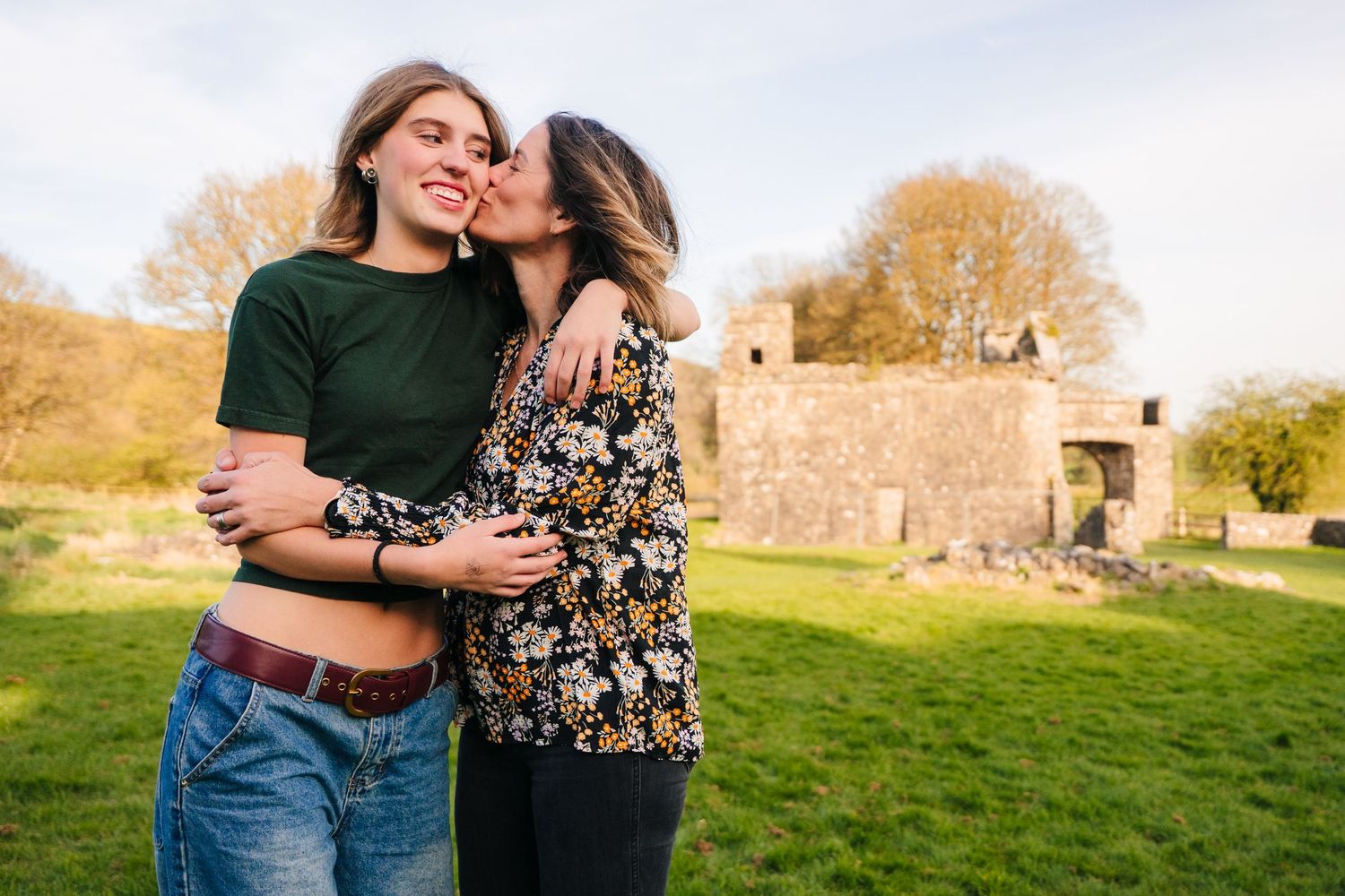 Two people share an intimate moment while standing in a grassy field with old stone ruins in the background. Photographer Ireland dublin