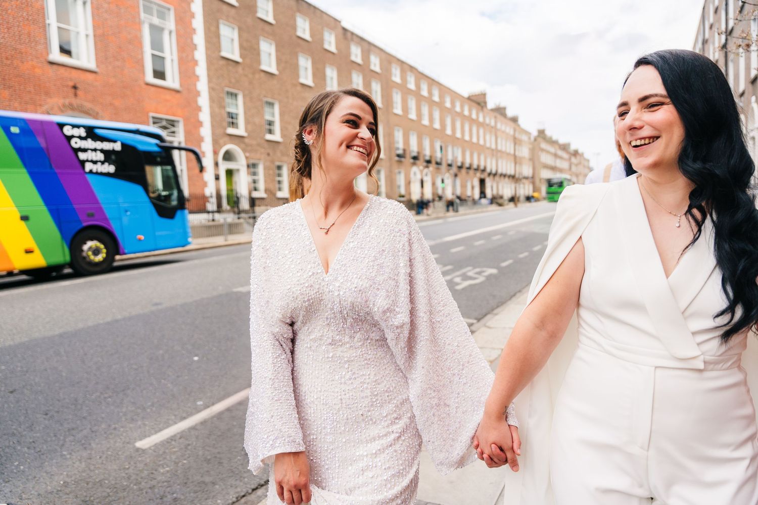 Row of white buildings line a street where people in light clothing walk together. House Dublin Wedding Photographer