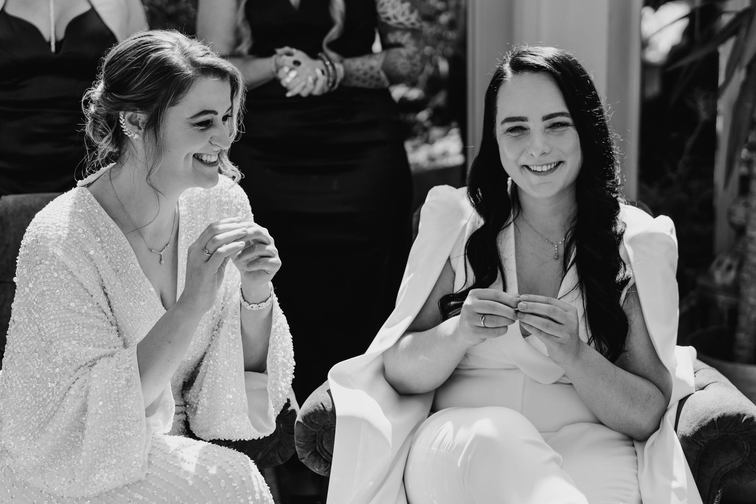 Two friends in white outfits share a laugh while sitting outdoors. House Dublin Wedding Photographer