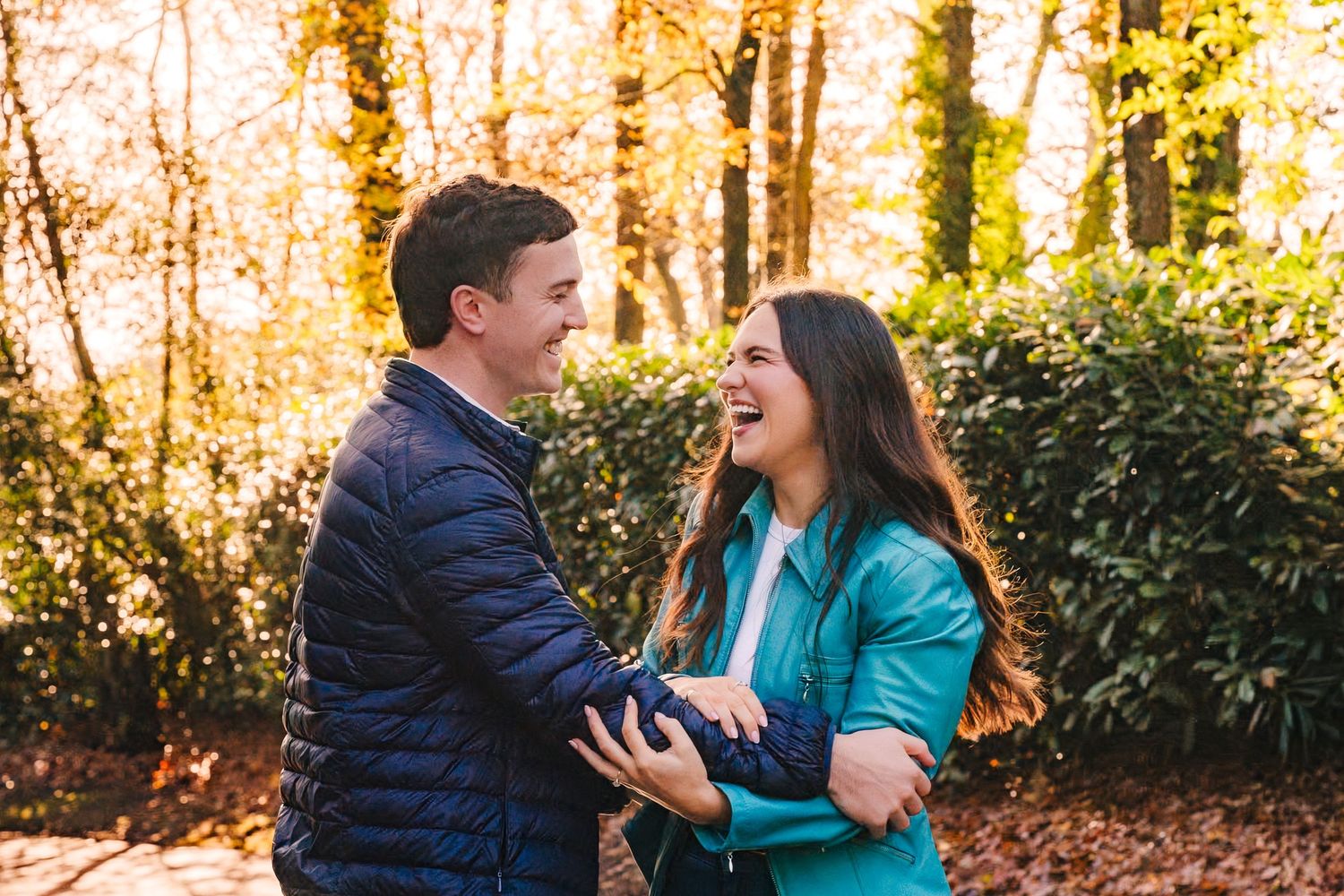 A couple in casual winter attire shares a joyful moment together in a sunlit wooded area during autumn. engagement photographer dublin