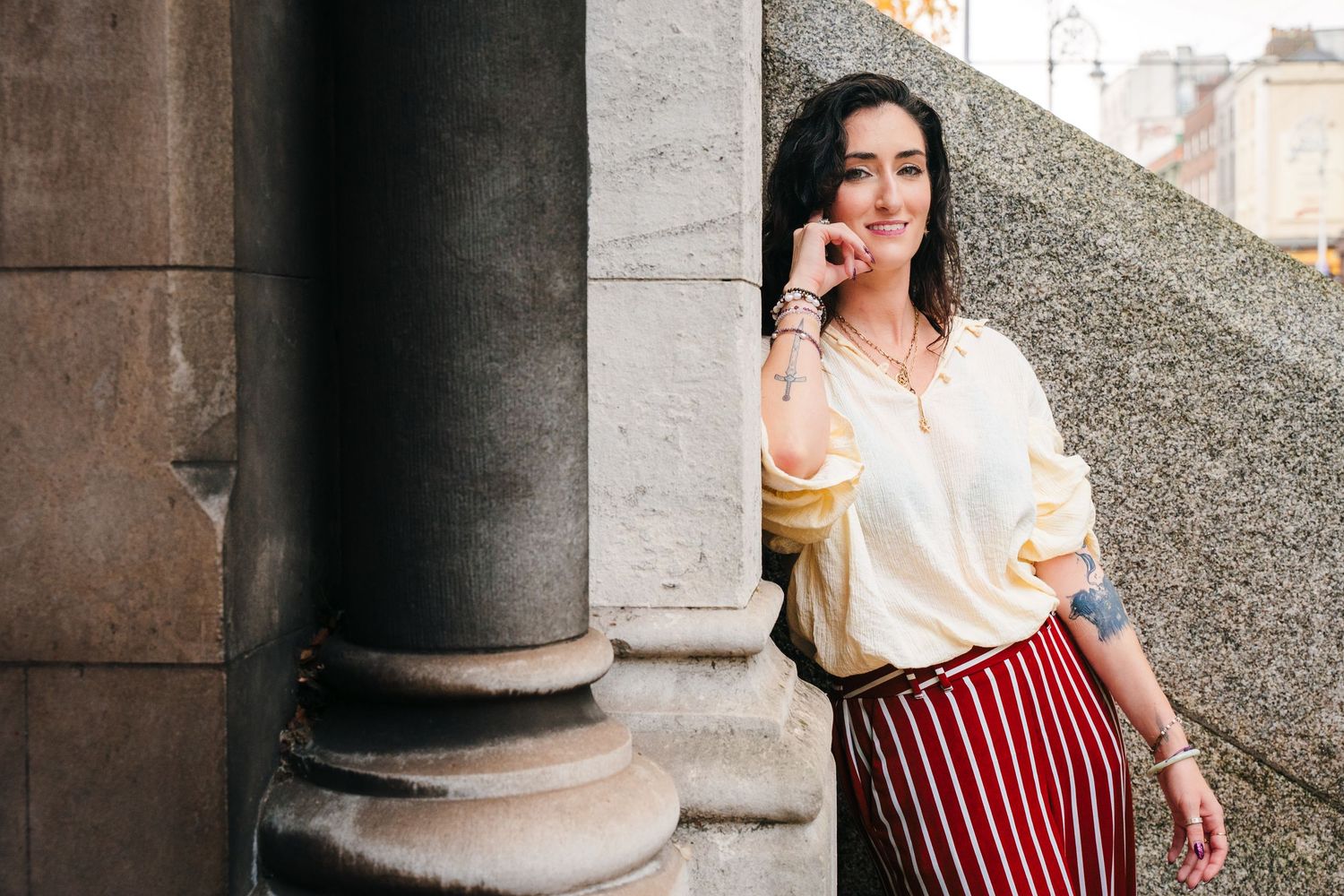Person in striped skirt and white blouse poses against stone columns on a city street. professional headshots dublin photographer