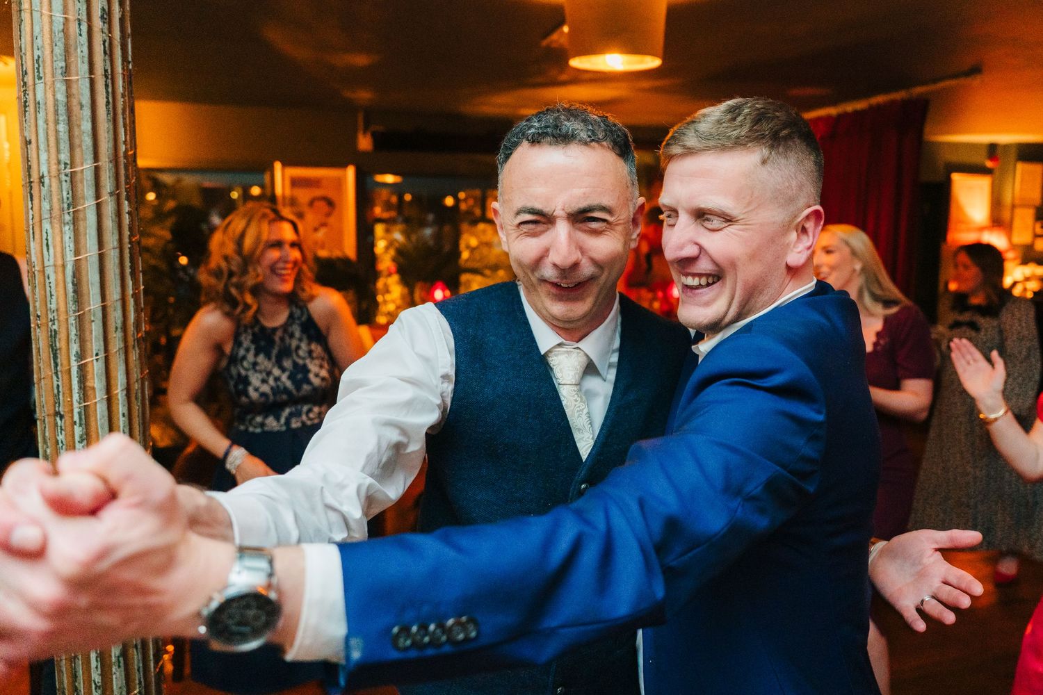 Wedding guests dancing and celebrating on the dance floor at an indoor reception with warm lighting.