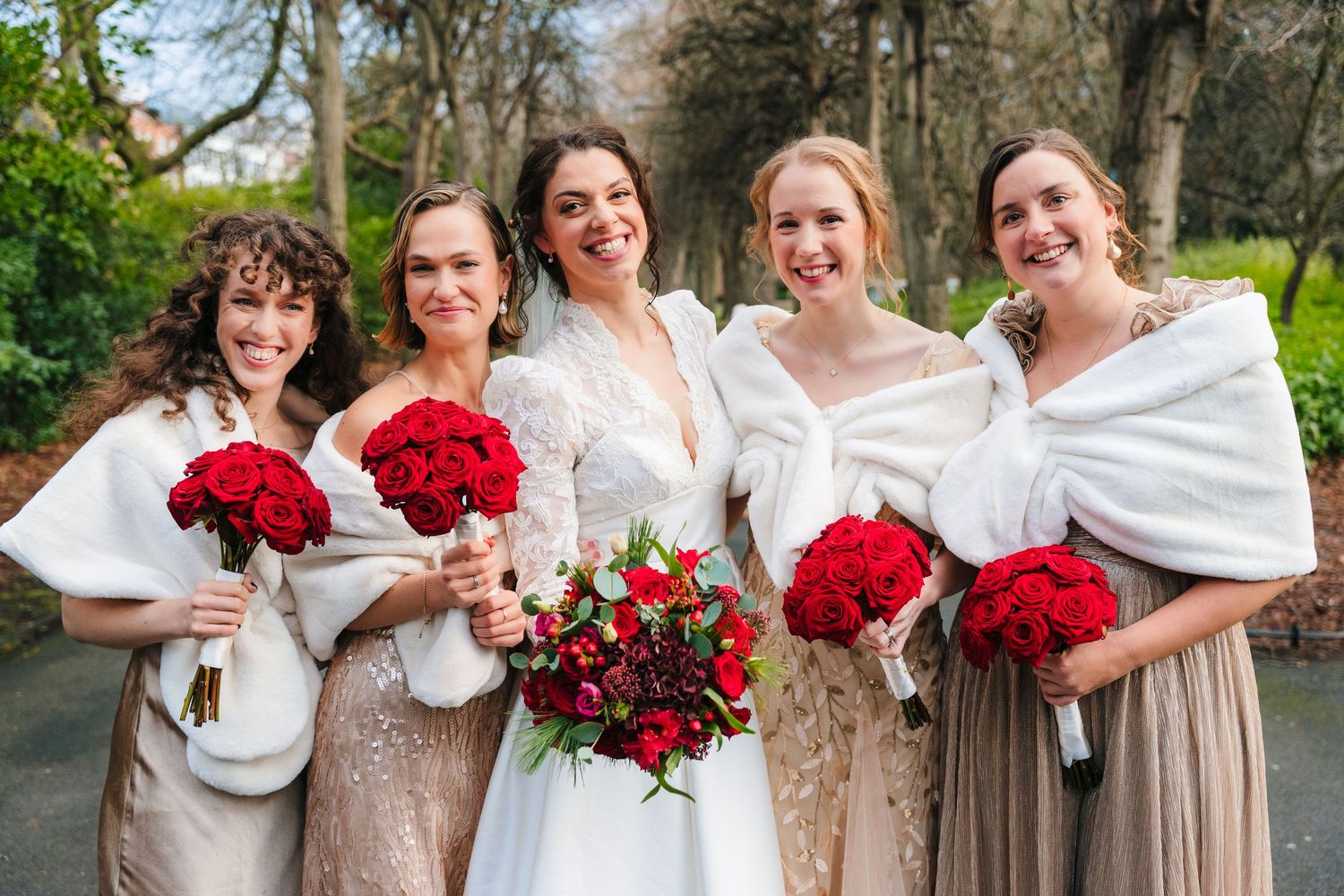 Wedding party wearing white shawls and holding vibrant red bouquets pose together outdoors. Stephens green club dublin Wedding photographer