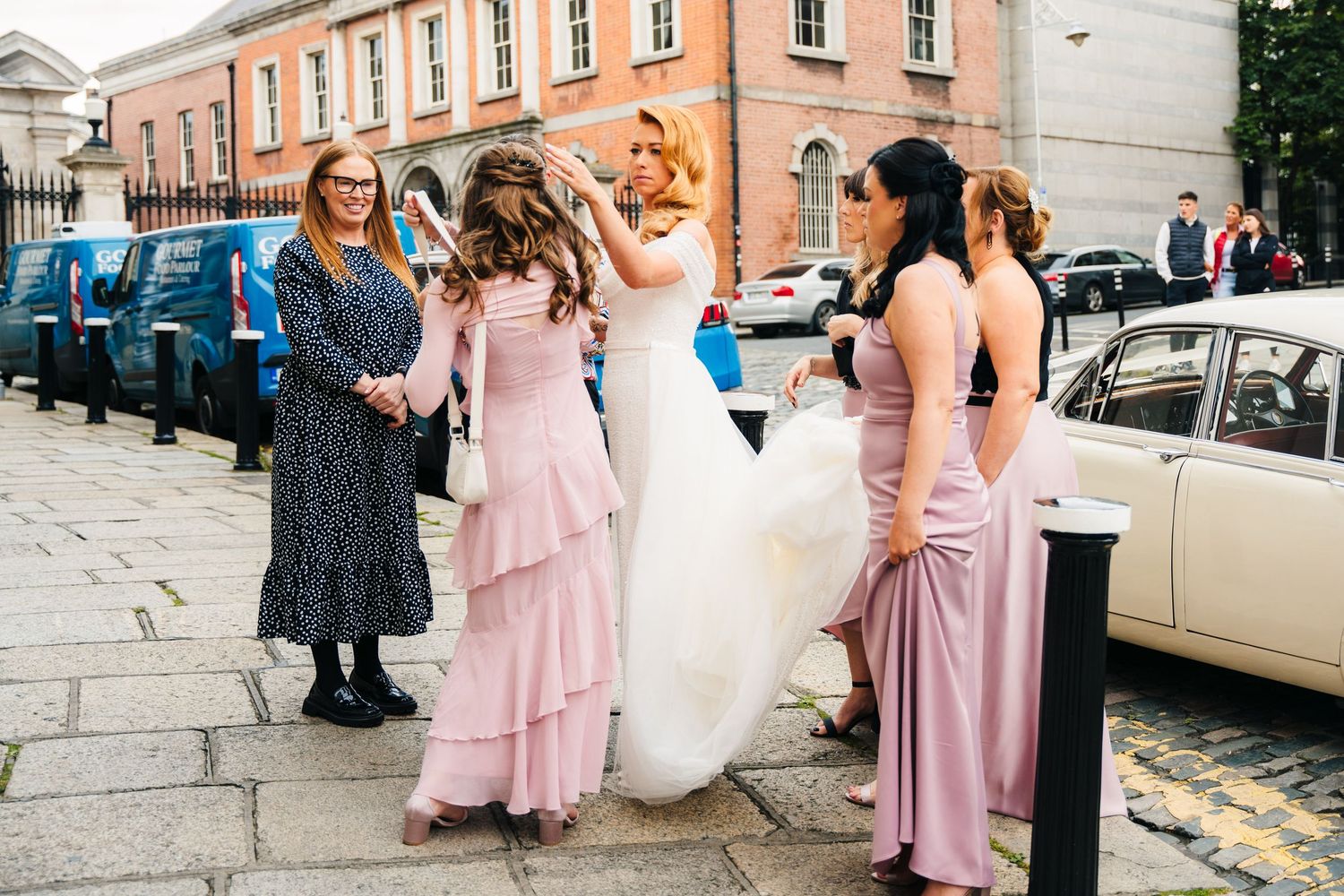 Wedding party in pink bridesmaid dresses and white bridal gown gather on stone steps for photos.  city hall dublin wedding photos