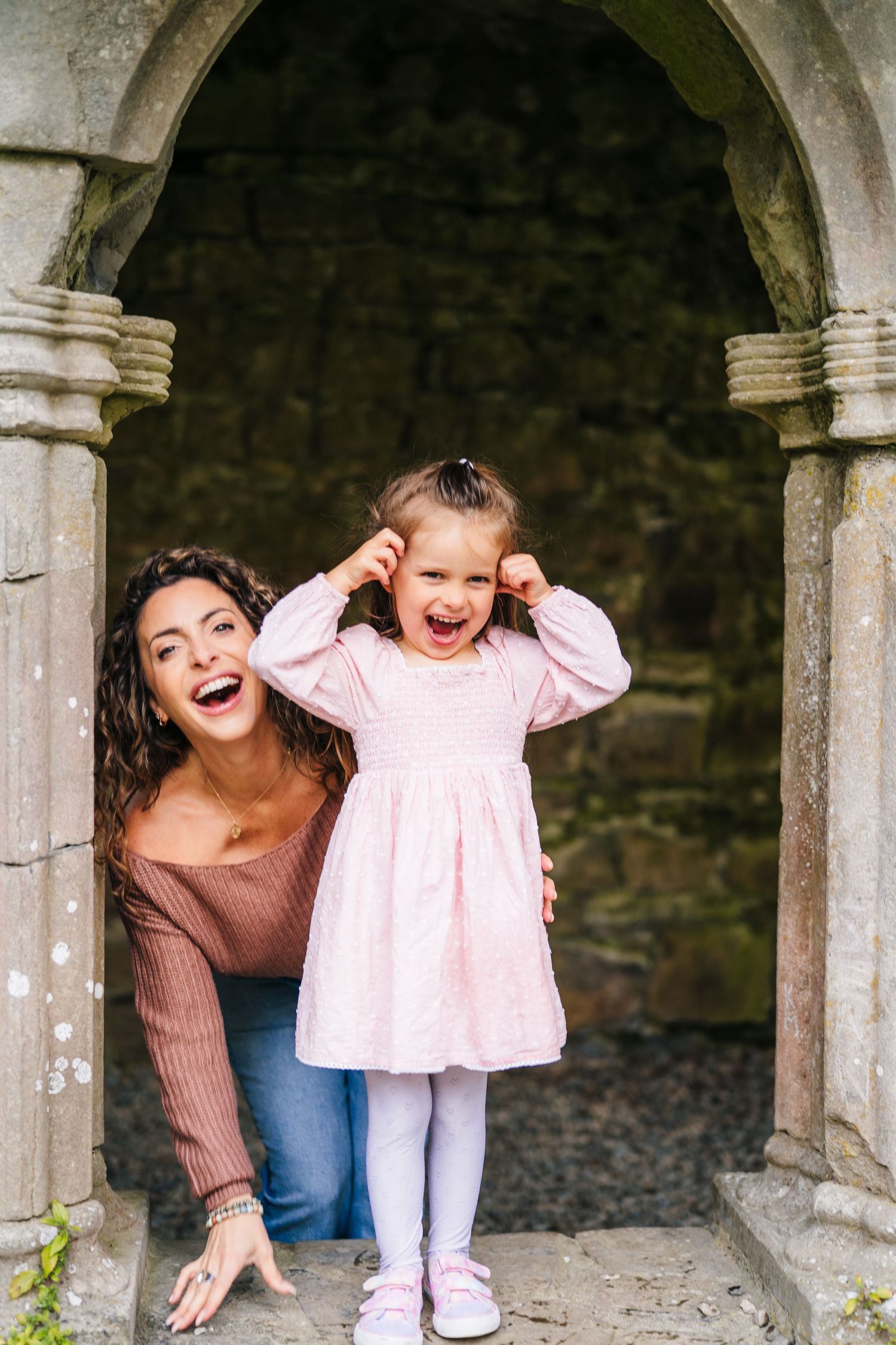 A joyful moment captured in a series of photos showing playful expressions through stone archways. Family photographer Dublin
