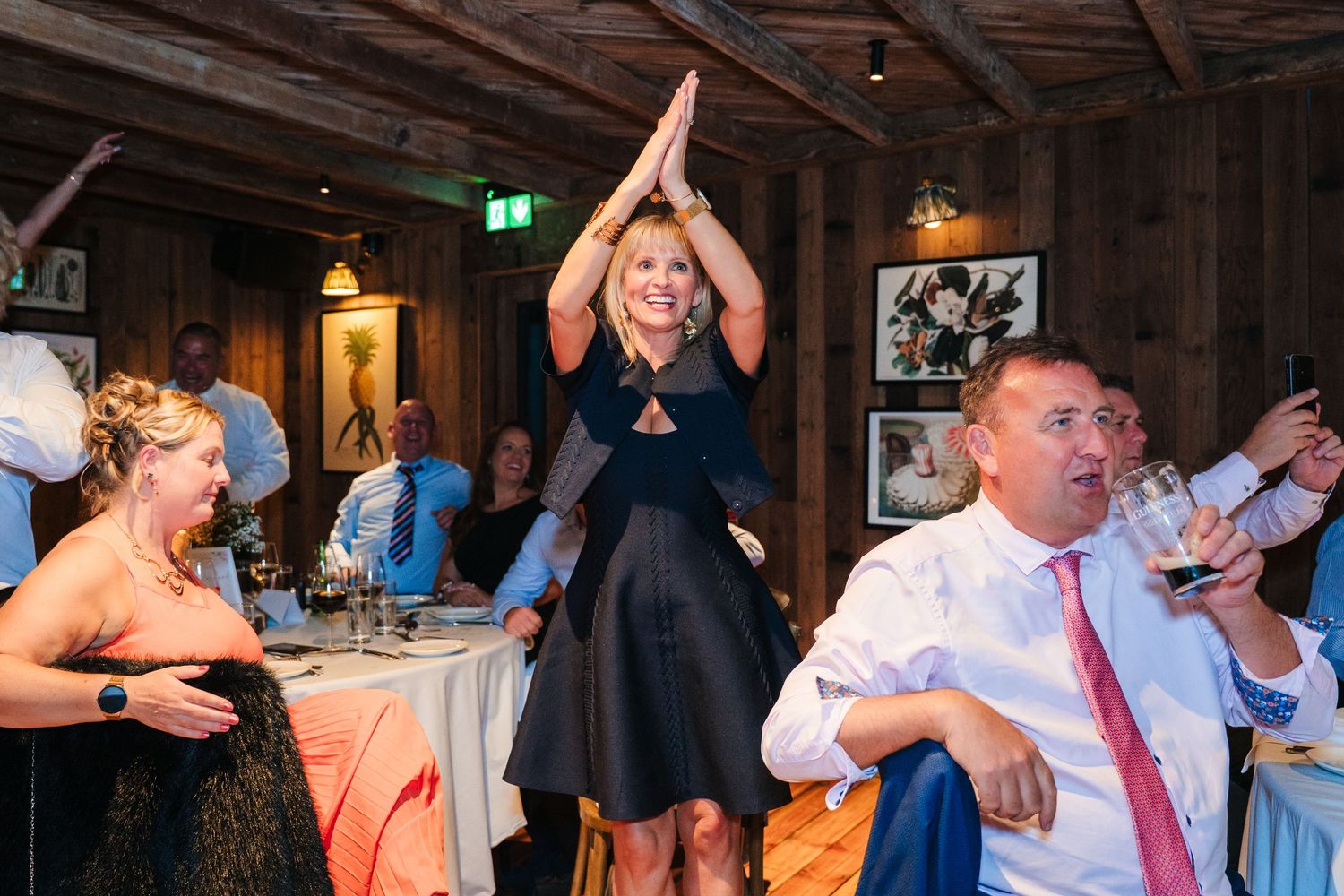 Wedding guests dancing and celebrating at a rustic indoor reception venue with wooden beams. The Dean Dublin Wedding Photographer