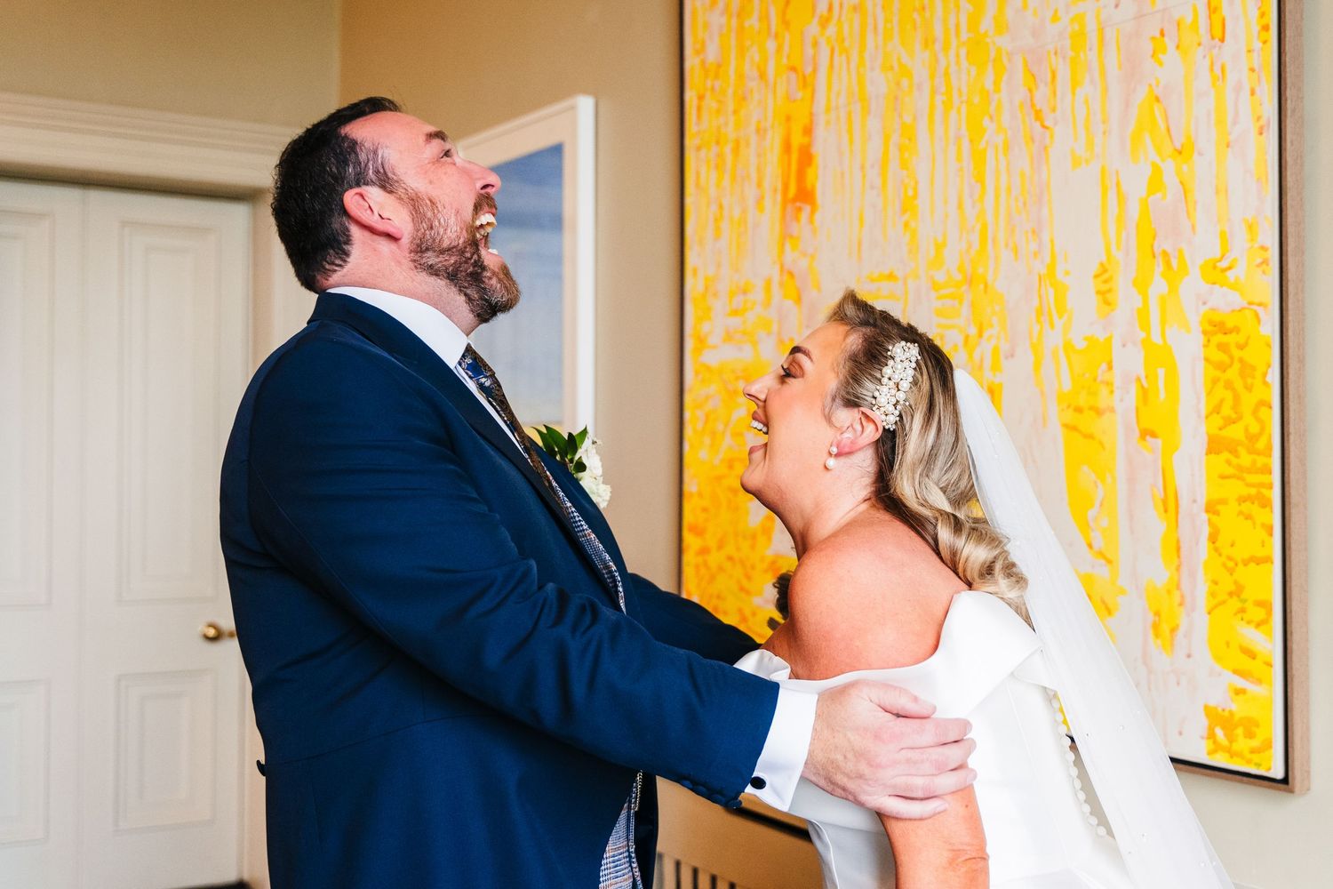 A couple shares a romantic moment during their wedding celebration against a bright yellow wall backdrop.