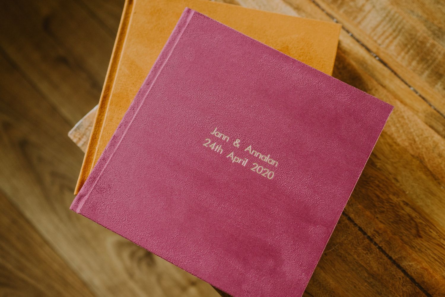 A pink wedding album book lies on a wooden surface showing different angles and perspectives.