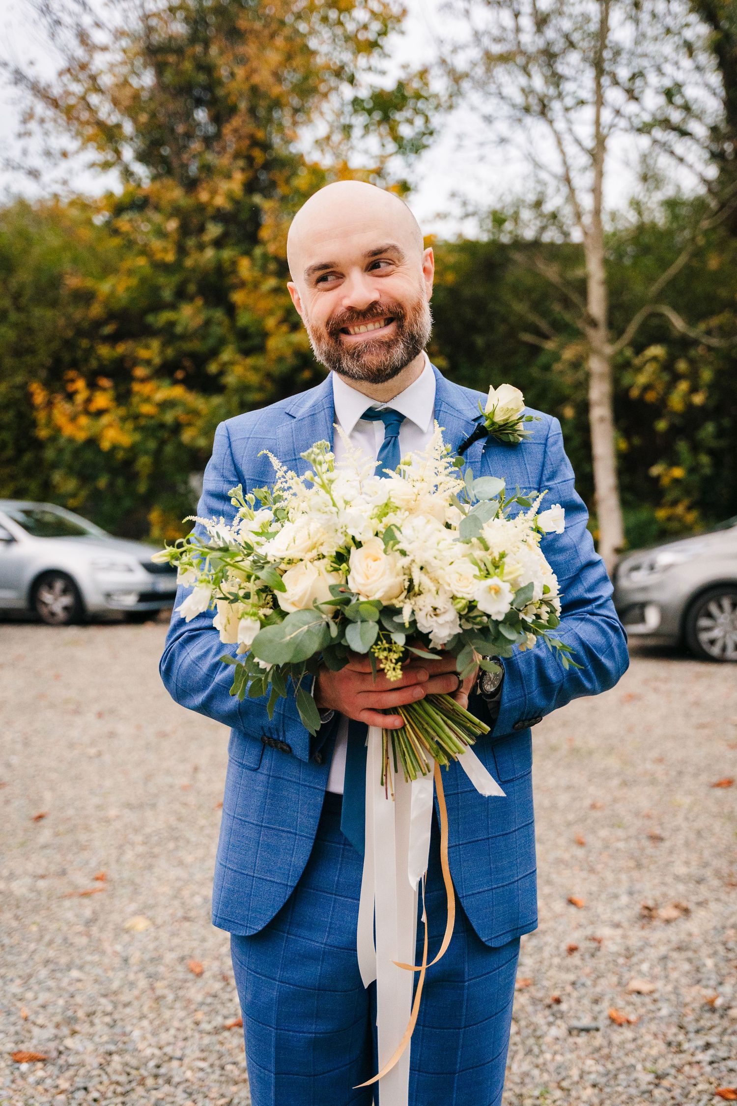Wedding attire featuring bright blue checkered suit with matching tie and beautiful white floral bouquet in outdoor setting. Wedding PHOTOGR