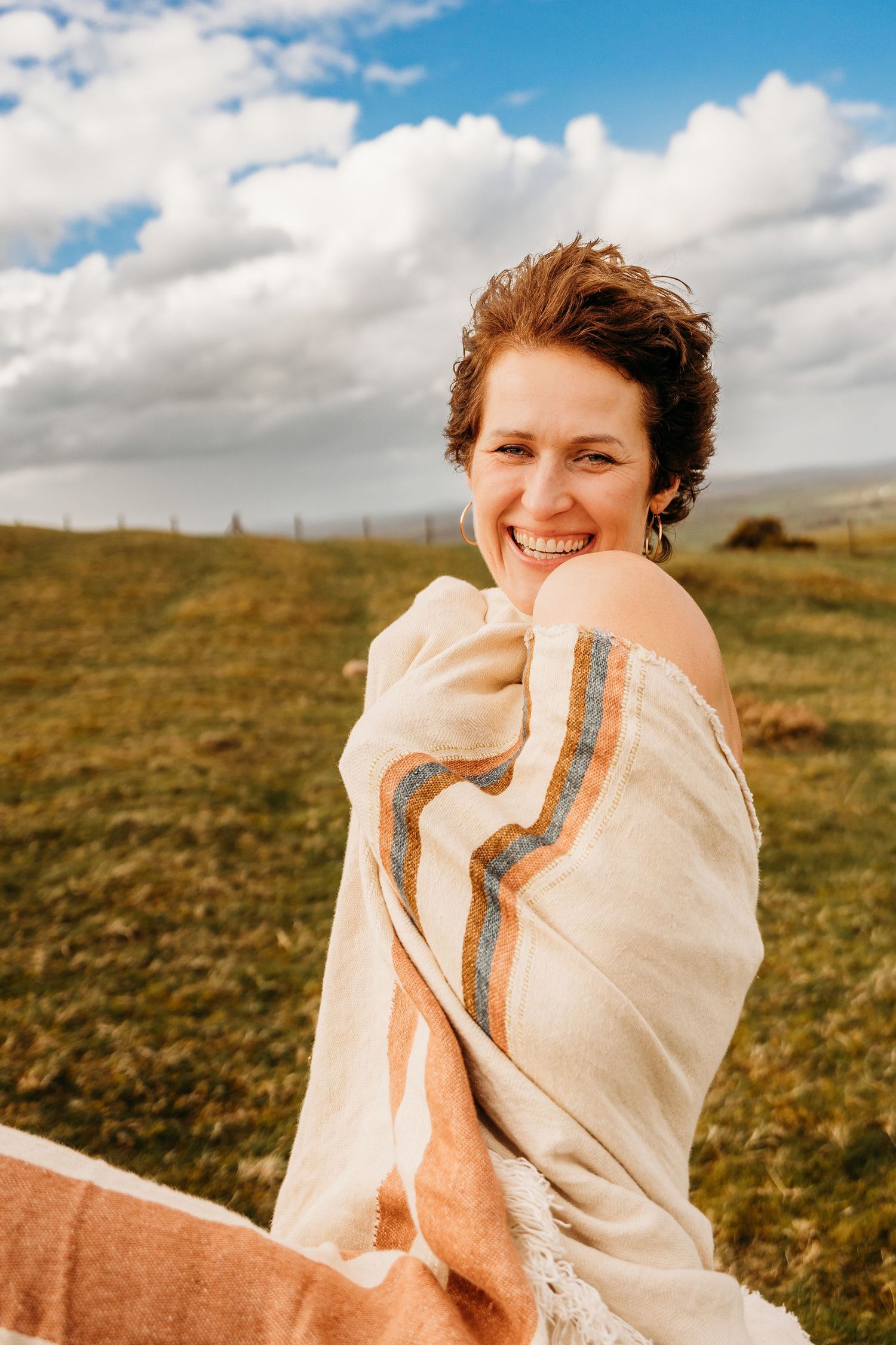 Someone is wrapped in a cream colored blanket while standing in a grassy field under a cloudy blue sky. Portrait PHOTOGRAPHER Dublin