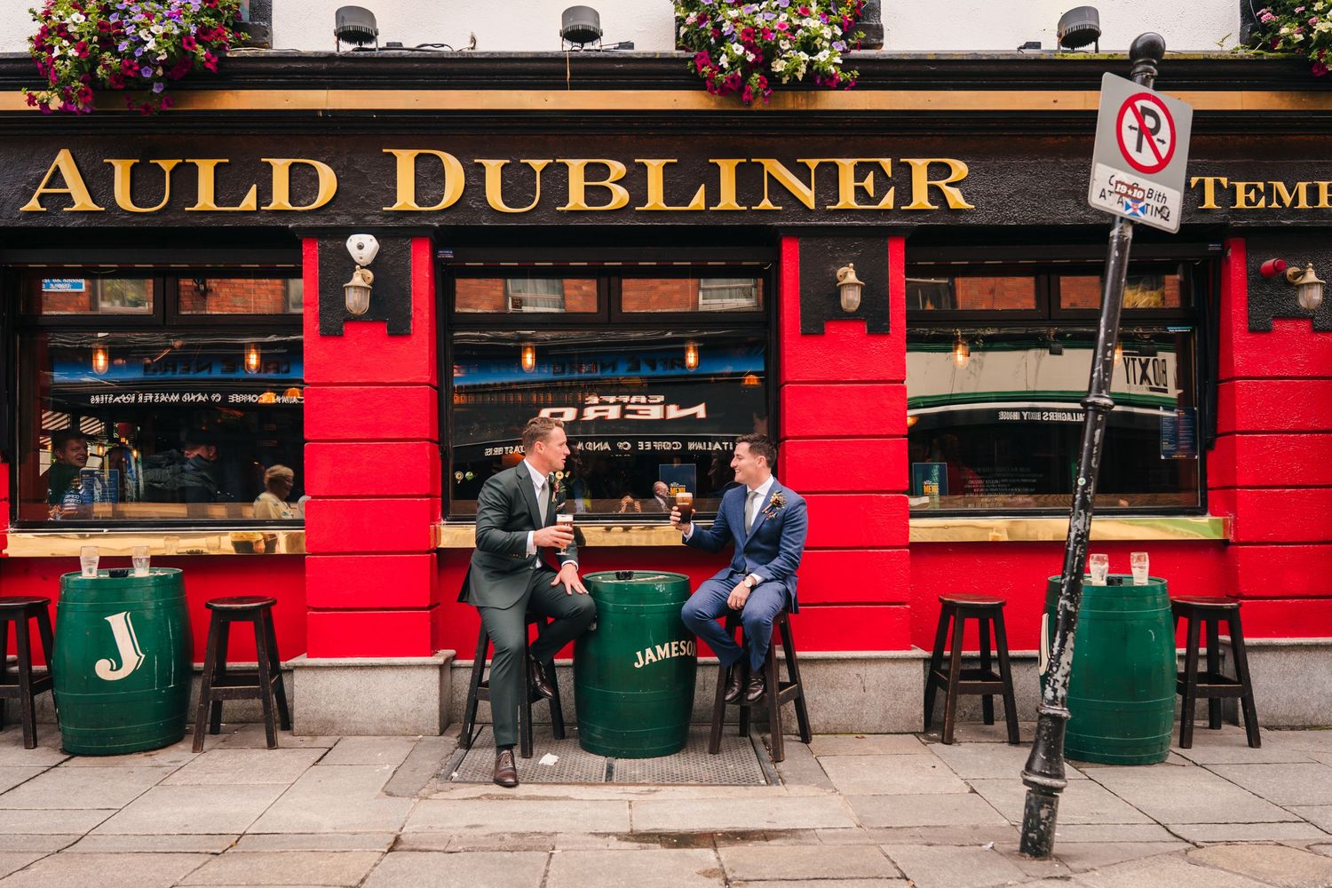 People sit outside the red-painted Auld Dubliner pub with green bins and flower baskets in Dublin, Ireland. Same sex wedding PHOTOGRAPHER Du