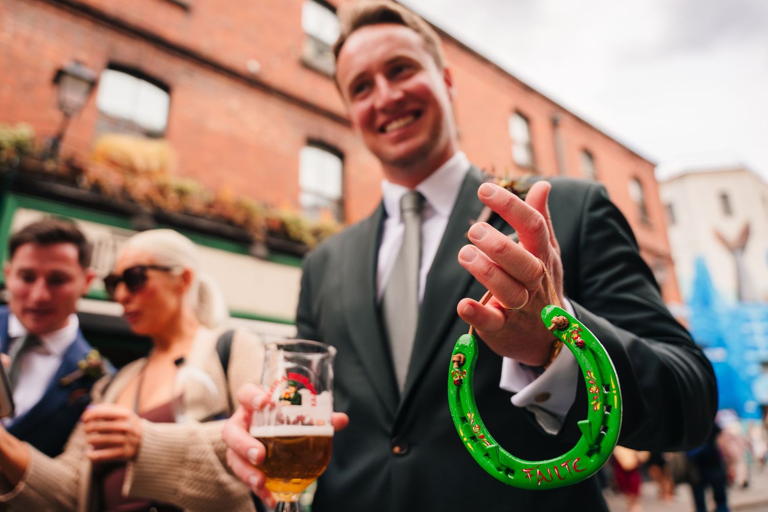 Someone in a gray suit holds a green horseshoe and beer glass during a festive outdoor celebration. Same sex wedding PHOTOGRAPHER Dublin