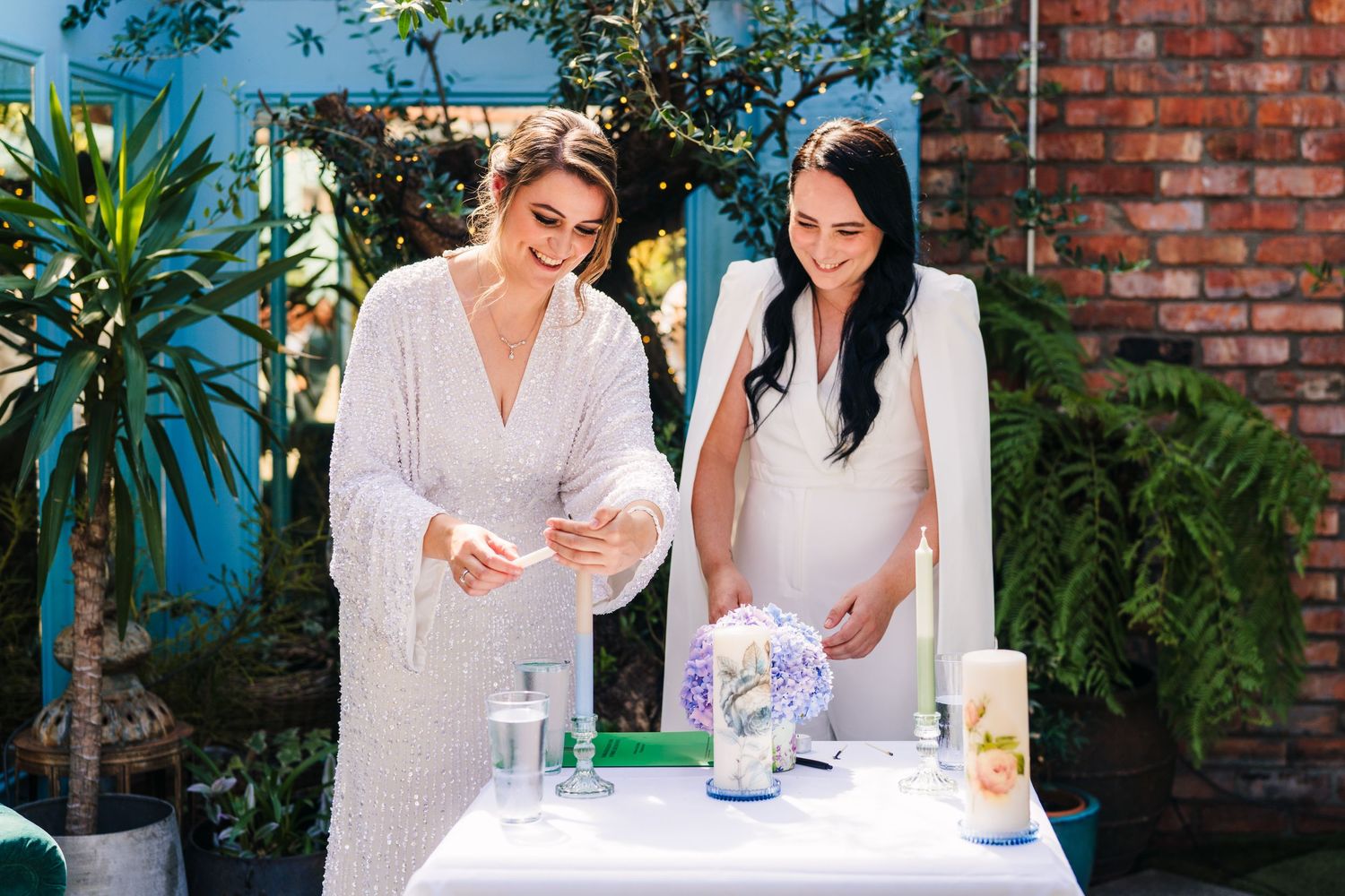 Women in white dresses socialize outdoors against rustic brick wall backdrop. House Dublin Wedding Photographer