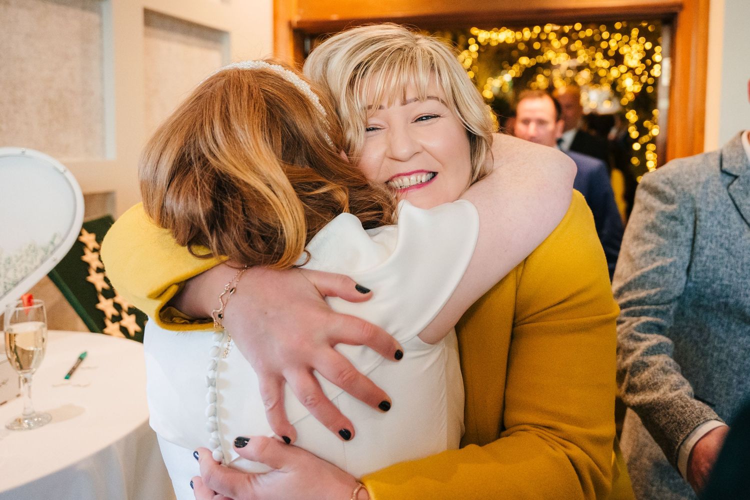 Two people share an emotional embrace at a celebration with twinkle lights in background.  Wedding PHOTOGRAPHER Trim Castle
