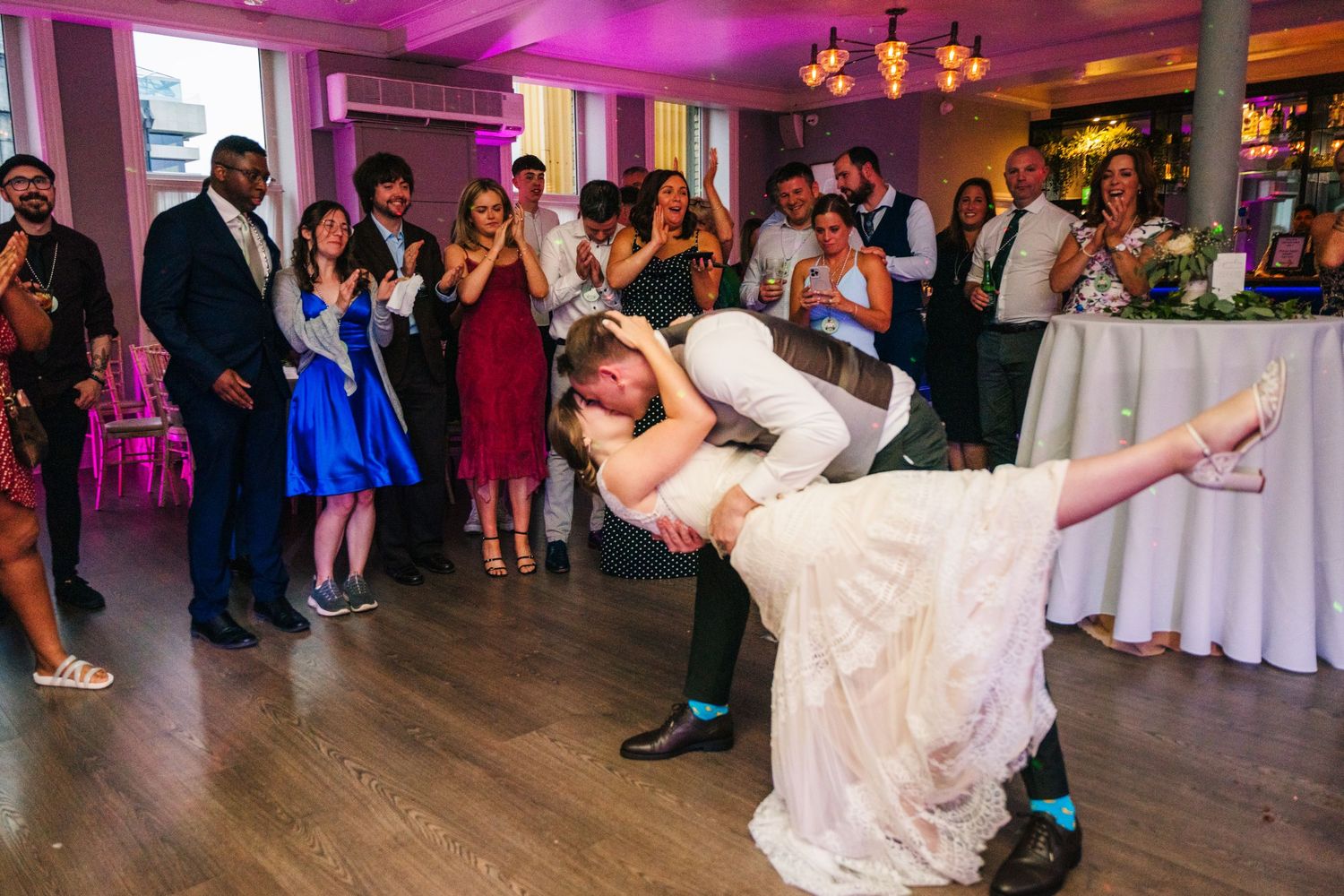 A dramatic dip during the first dance at a wedding reception with purple lighting and guests watching. PHOTOGRAPHER Dublin Ireland Wedding