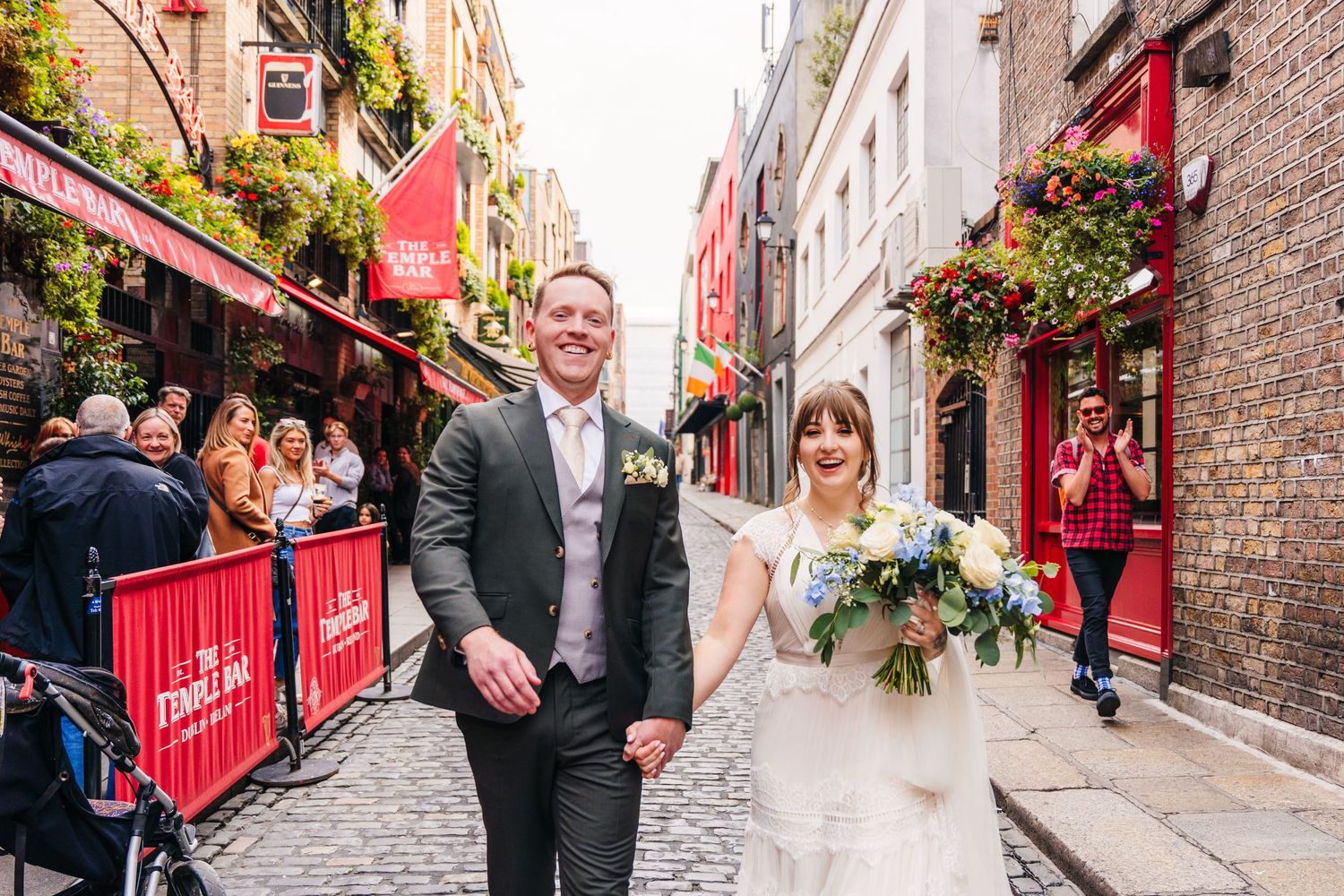 Couple walking through cobblestone street with red pub facades and hanging flowers. PHOTOGRAPHER Dublin Ireland Wedding
