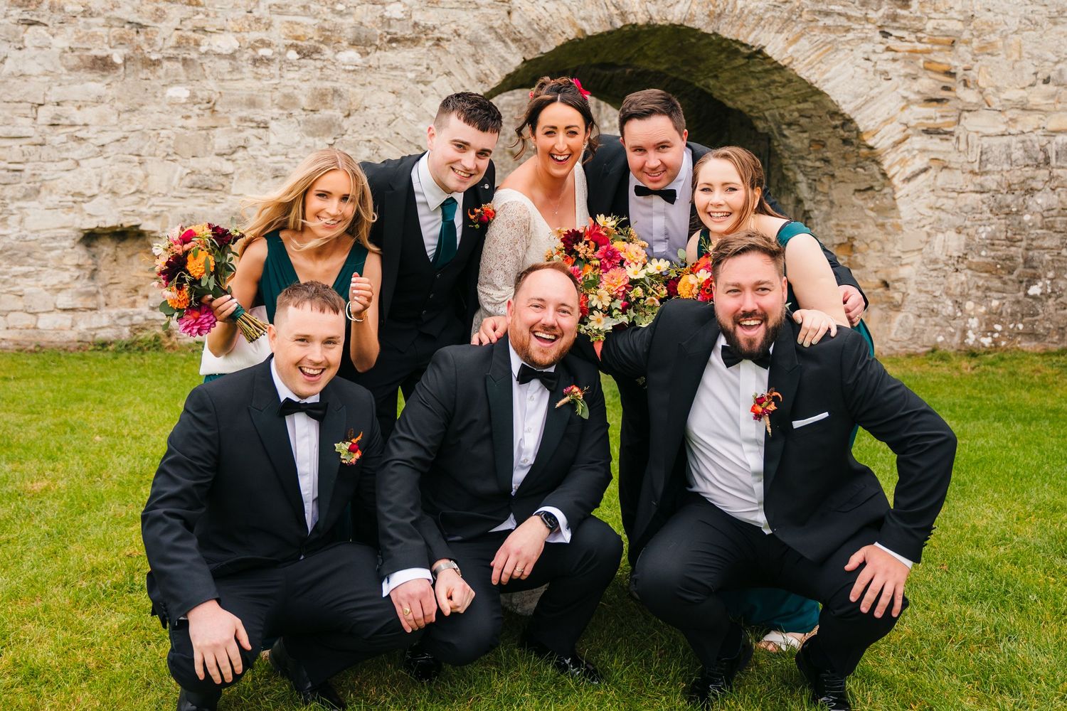 Wedding party poses casually against stone wall backdrop outdoors. Wedding Photography Trim Castle Ireland