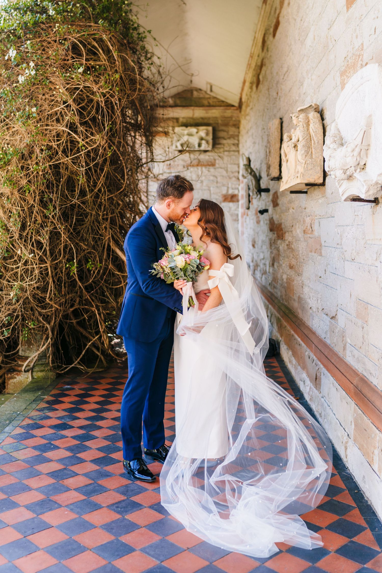 Castle Leslie Wedding Photographer Dublin Newlywed couple embraces in a rustic hallway with checkered floor tiles and trailing veil.