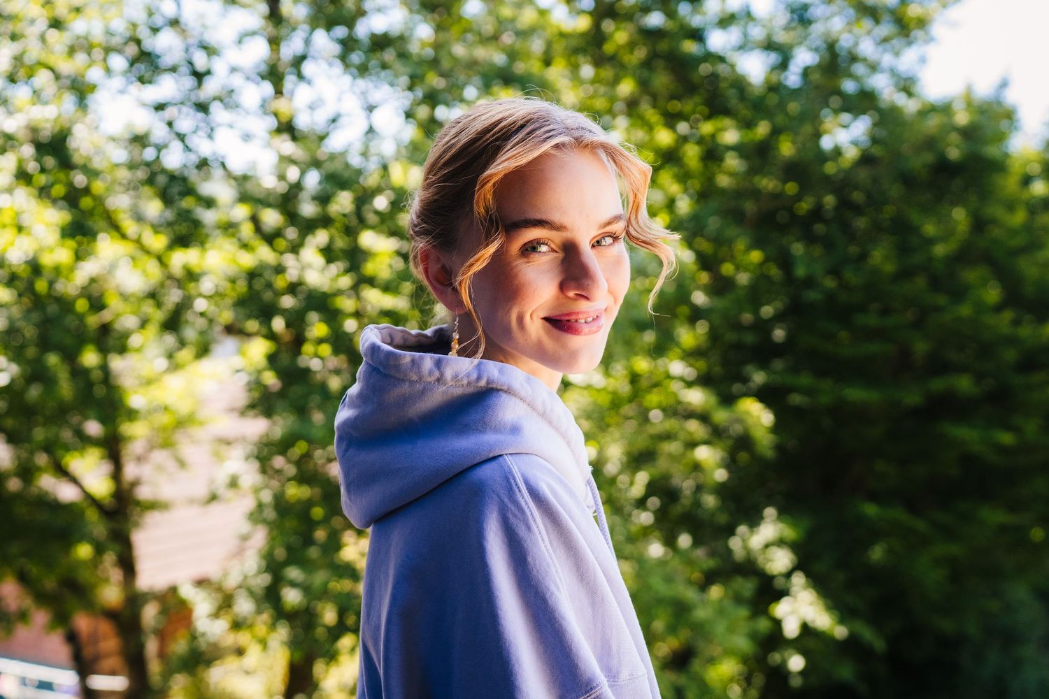 Someone wearing a light blue hoodie smiles while looking back over their shoulder in a sunny outdoor setting. Poulaphouca Wedding photograph