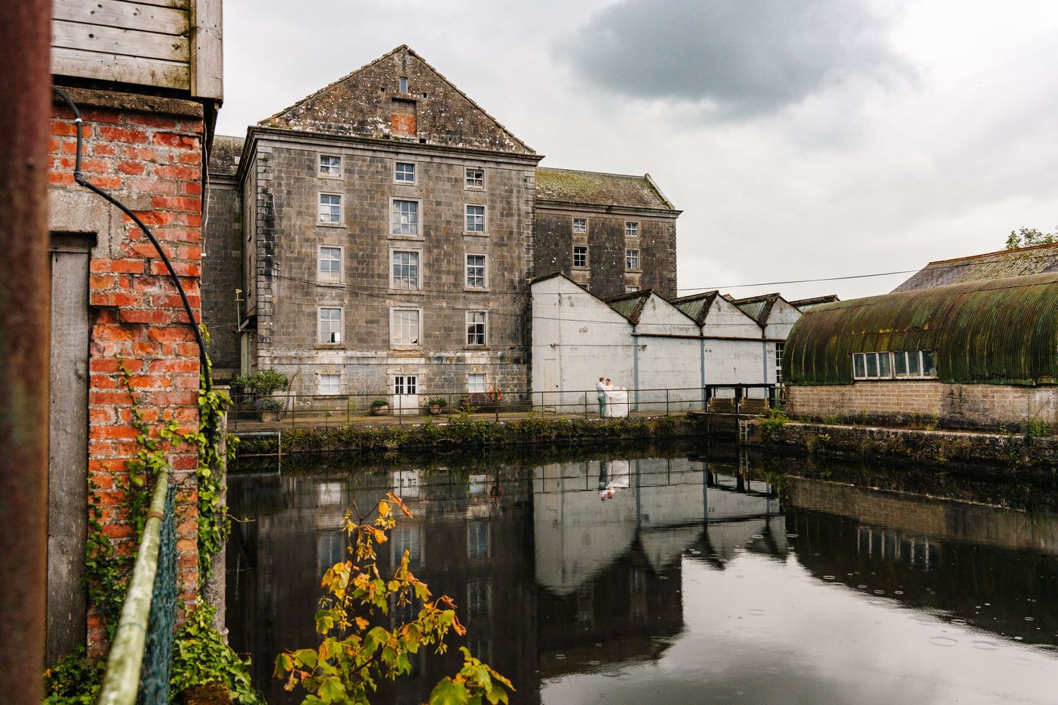 Millhouse slane wedding photographer Industrial warehouse buildings reflect in still canal waters against cloudy skies in historic district.