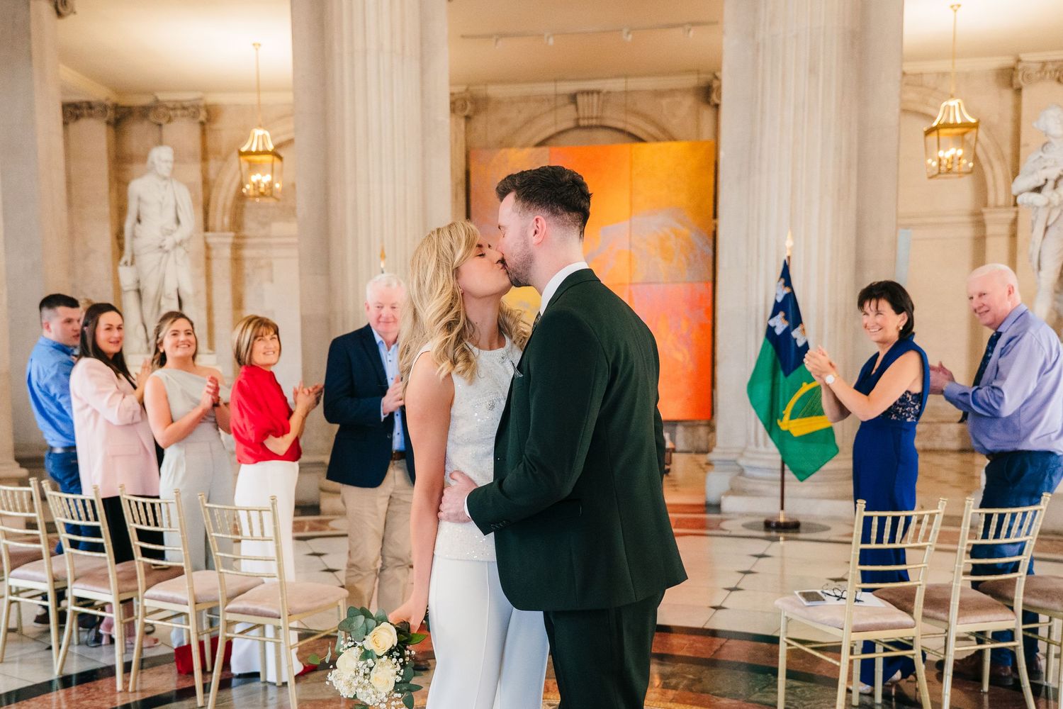 A wedding celebration in an elegant columned hall with guests standing and national flags on display. City Hall Dublin wedding photogrAPher