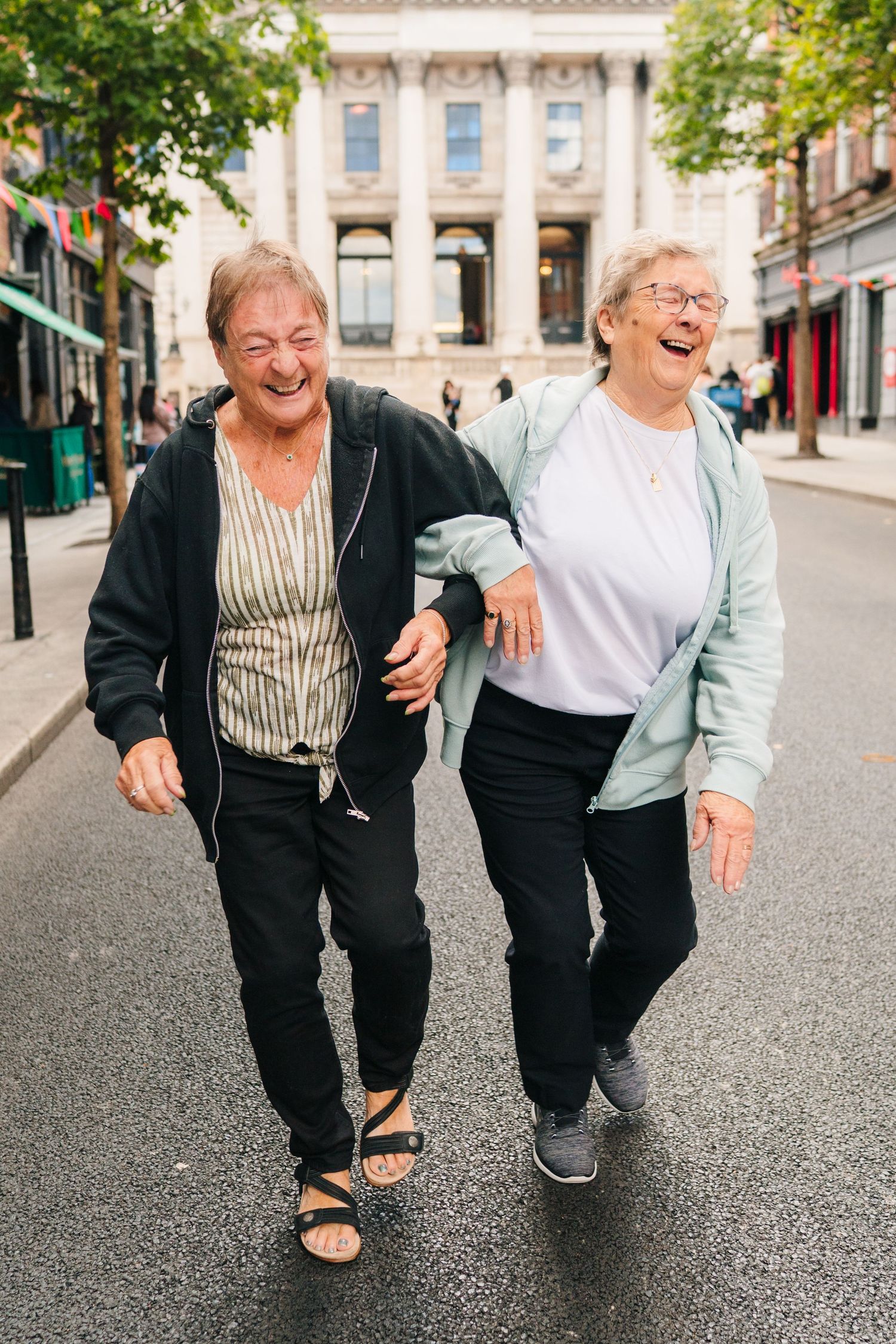 Two seniors share a joyful moment together while walking outdoors on a city street. Family photographer dublin