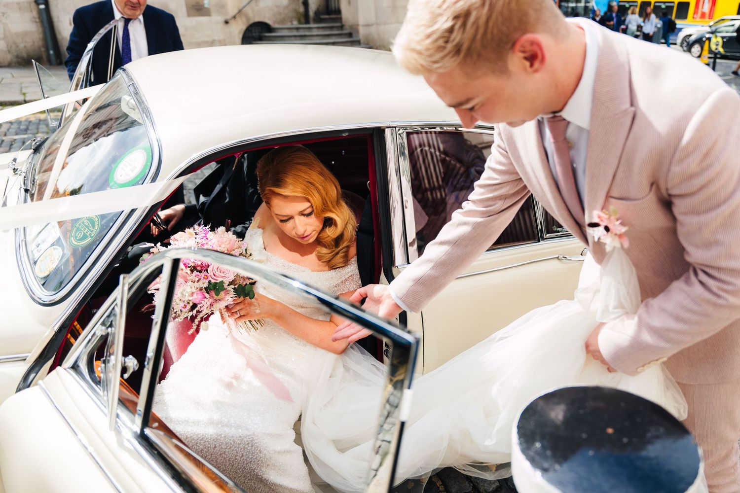 Bride in white dress enters classic car while being assisted on wedding day.  city hall dublin wedding photos