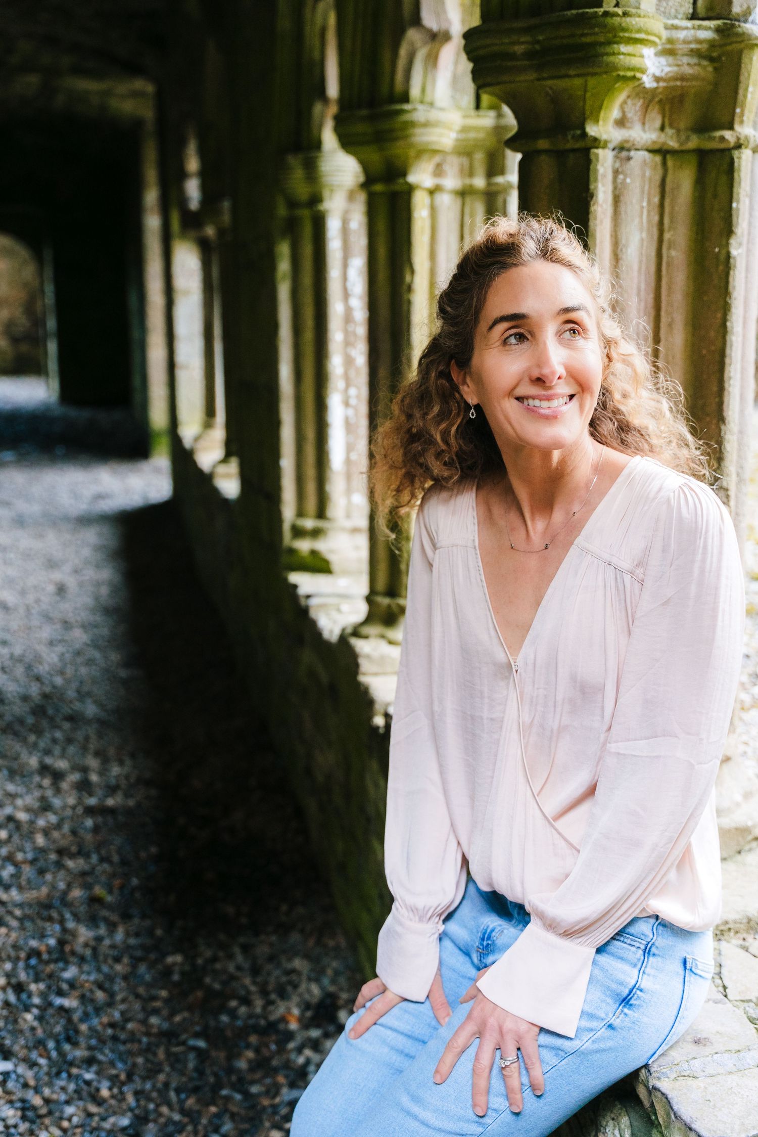 Person in white blouse sitting by stone columns in a historic cloister.BEctive abbey family photographer dublin