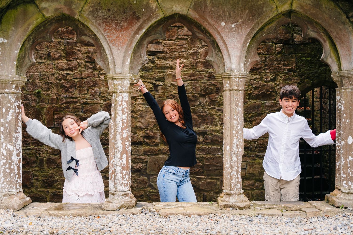 A sequence of playful poses along a stone wall archway in a historic setting. BEctive abbey family photographer dublin