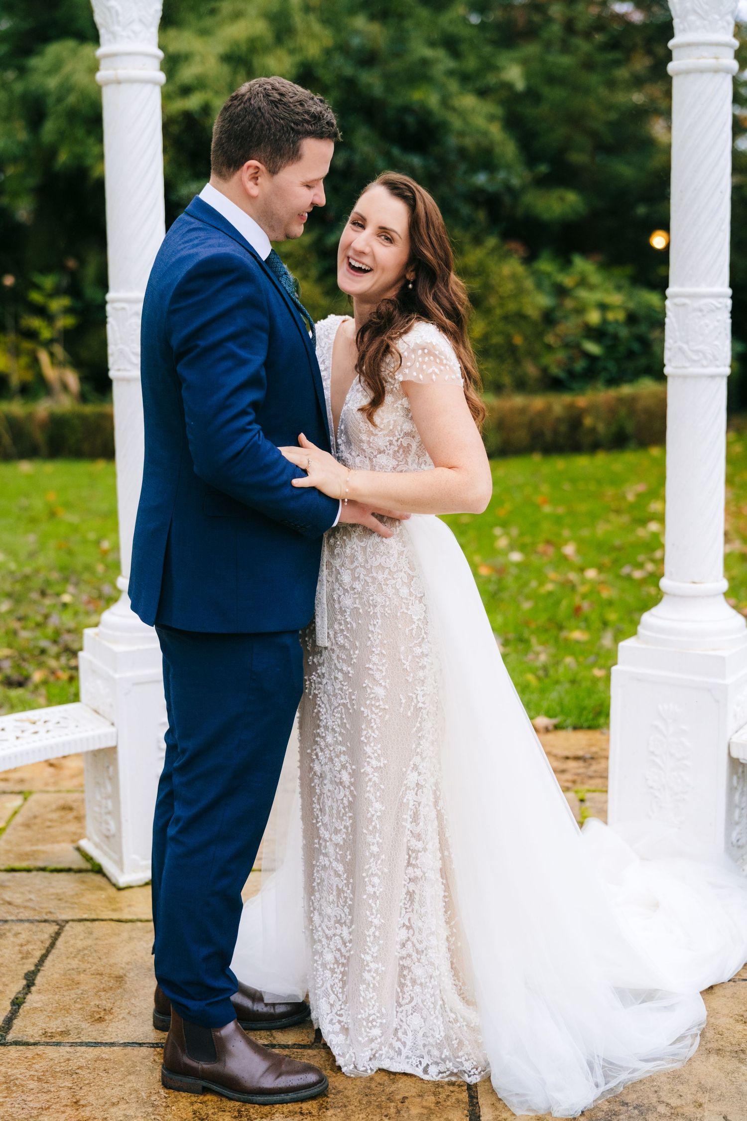 Romantic moment captured between couple by white pillars in an outdoor garden setting.